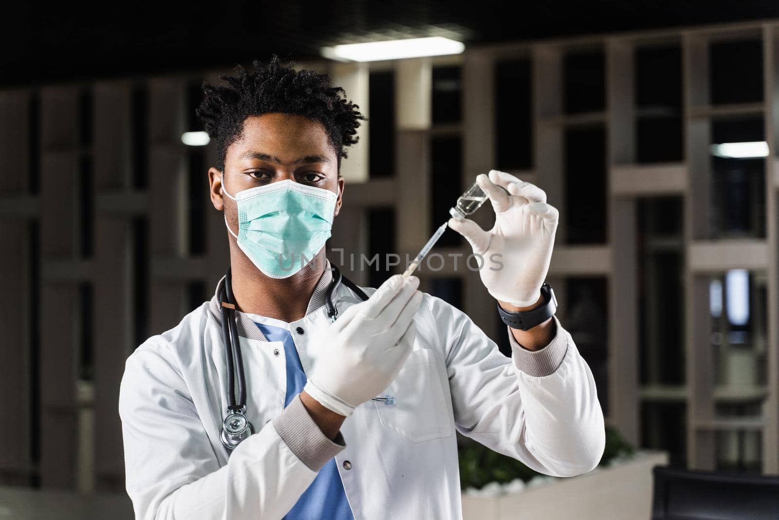 African doctor in a medical mask prepares to inject coronavirus covid-19 vaccine. Black doctor in white medical robe with syringe for making vaccination. by Rabizo