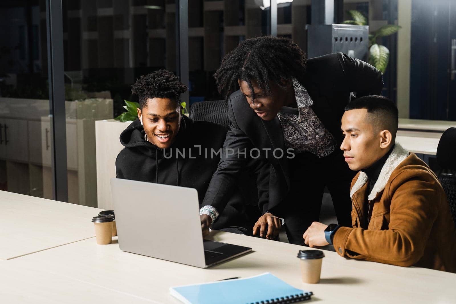 Multiethnic group of African and Asian colleagues are working on laptop on business project. Two black handsome managers teamwork with an Asian man and create creative ideas