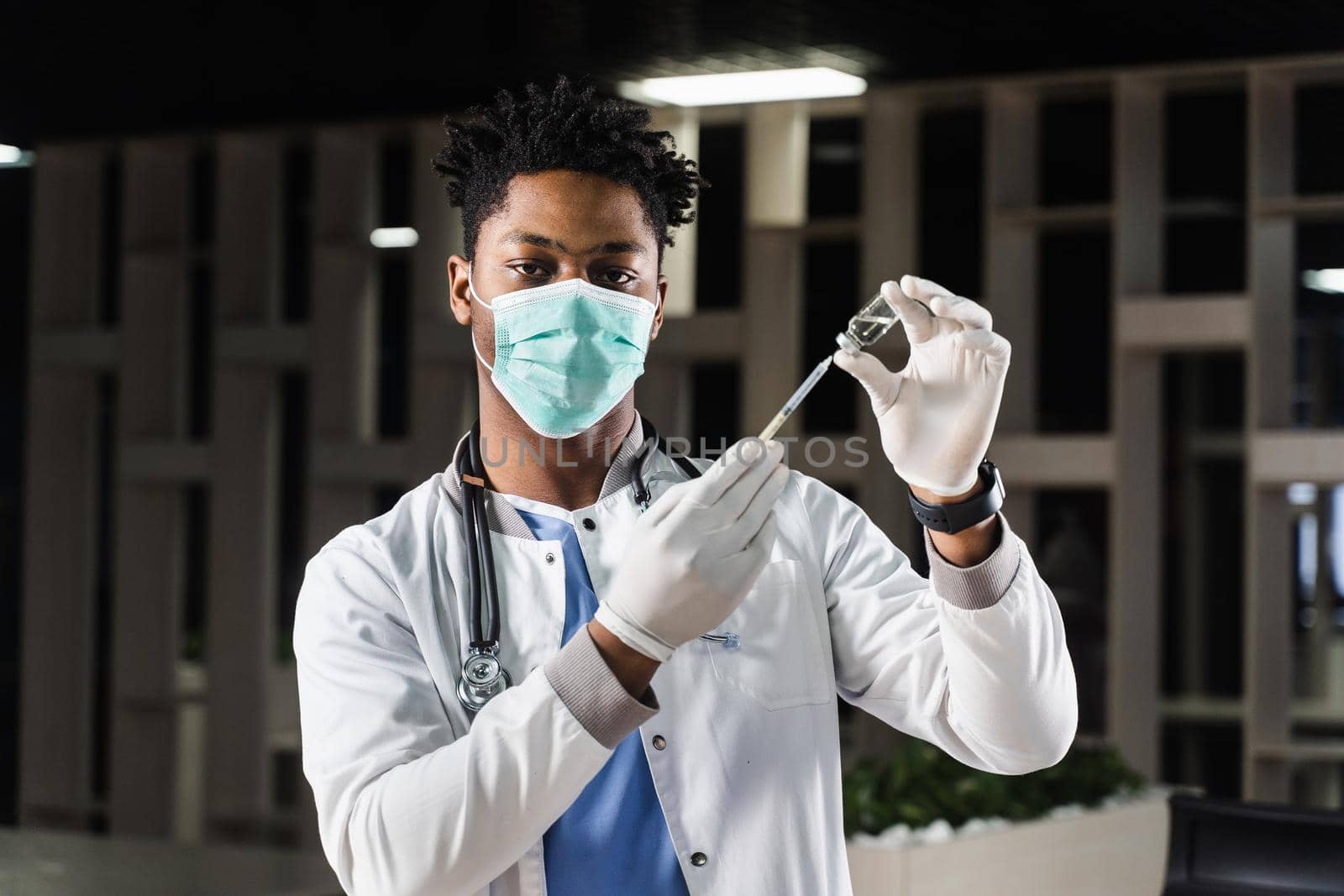 African doctor in a medical mask prepares to inject coronavirus covid-19 vaccine. Black doctor in white medical robe with syringe for making vaccination. by Rabizo