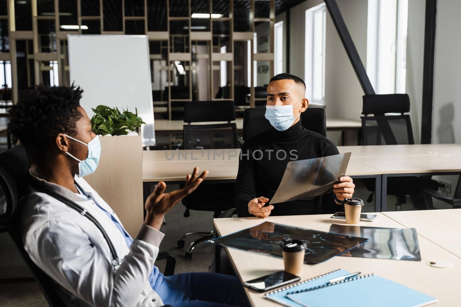 Handsome asian patient with x-ray image of fracture of foot bones at black doctor consultation. African surgeon discussing x-ray with patient