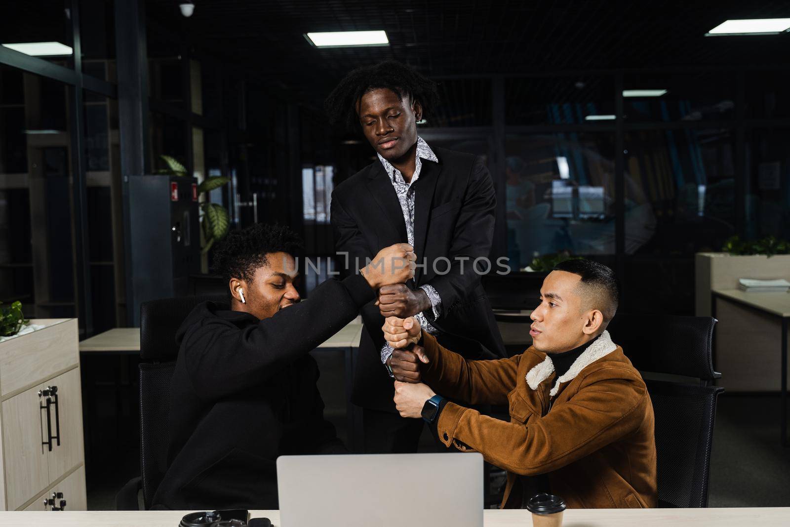 Multiethnical diverse colleagues making hand stack of fists. Black africans and asian working online with laptop in office. by Rabizo