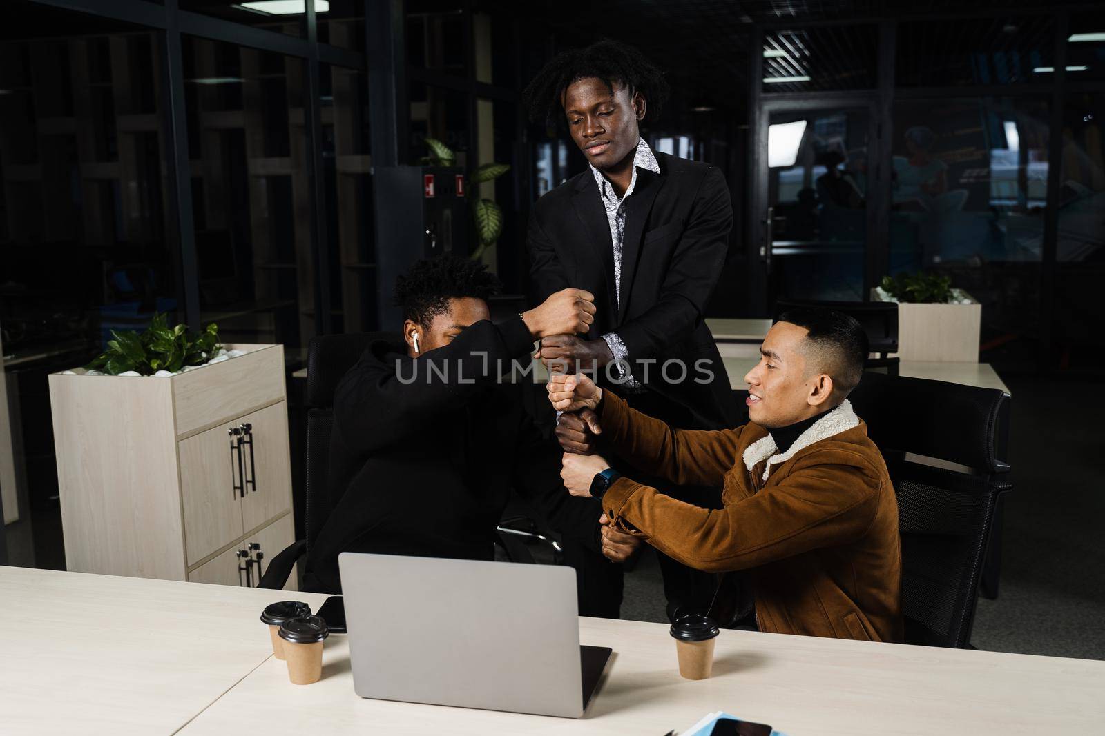 Multiethnical diverse colleagues making hand stack of fists. Black africans and asian working online with laptop in office. by Rabizo