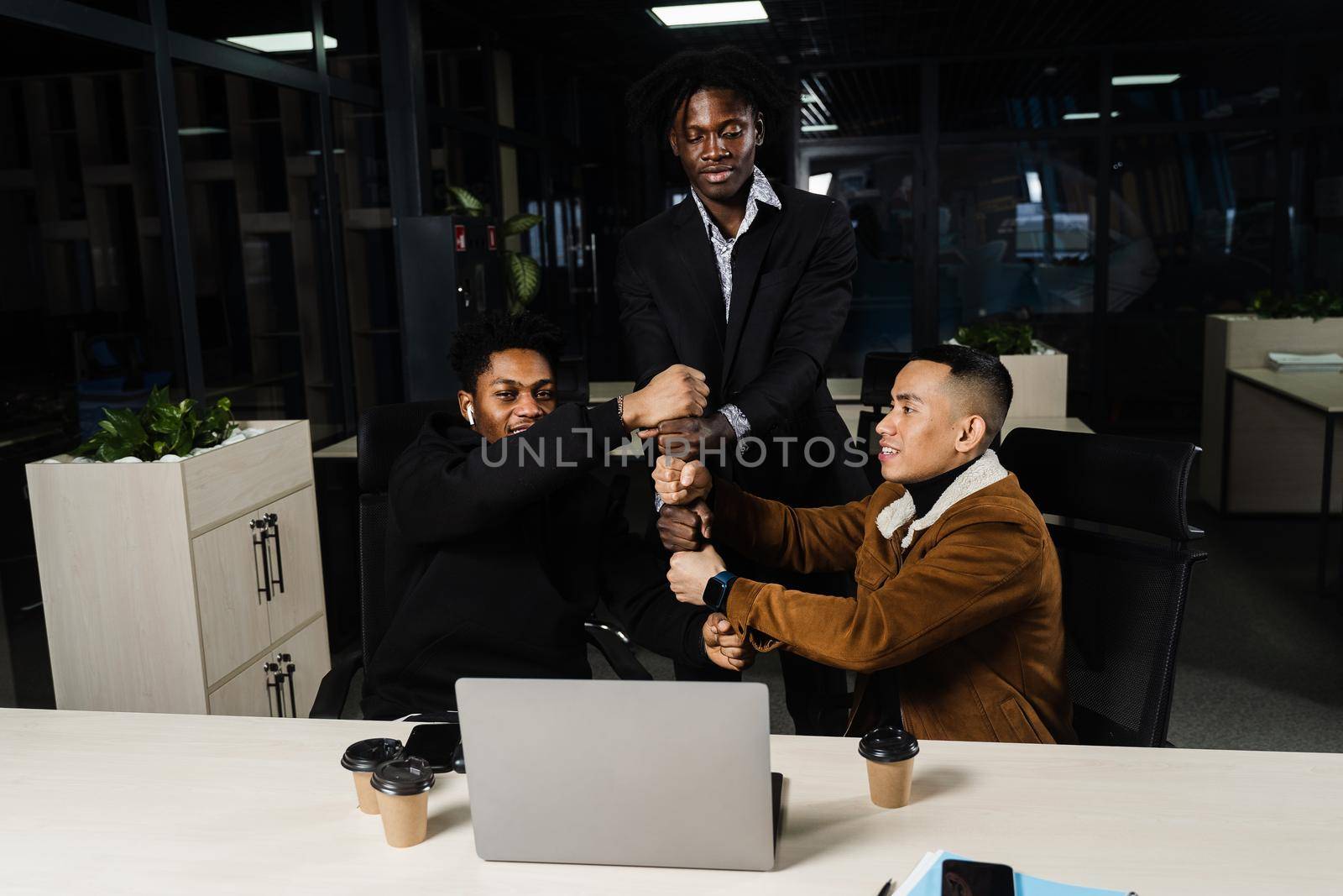 Multiethnical diverse teamwork online with laptop. African and Asian colleagues making hand stack of fists. Community spirit and friendship. Keeping high motivation