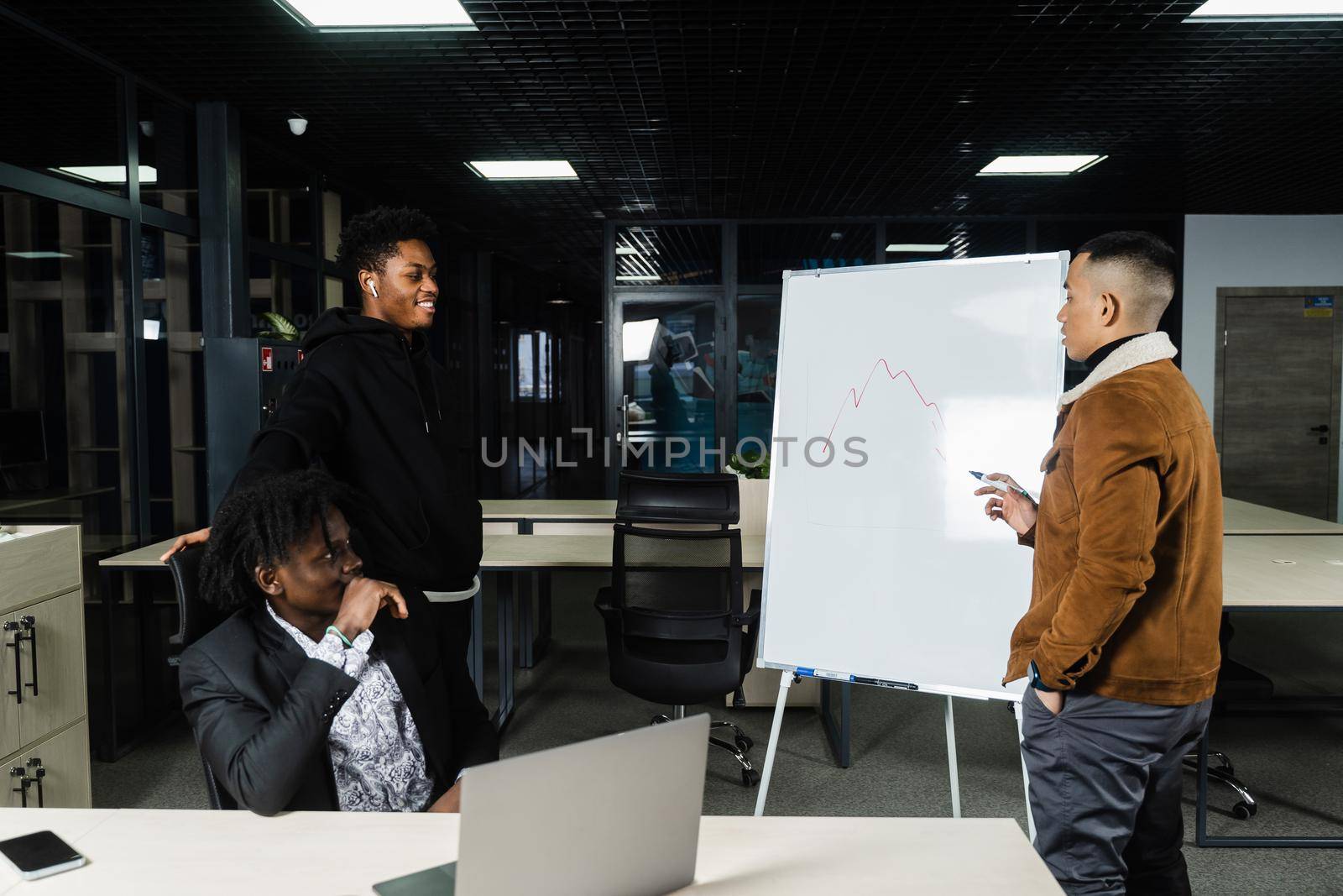 Multiethnic investors are discussing graph of cryptocurrencies and bitcoin. Black African and Asian businessmen are discussing economic financial situation together