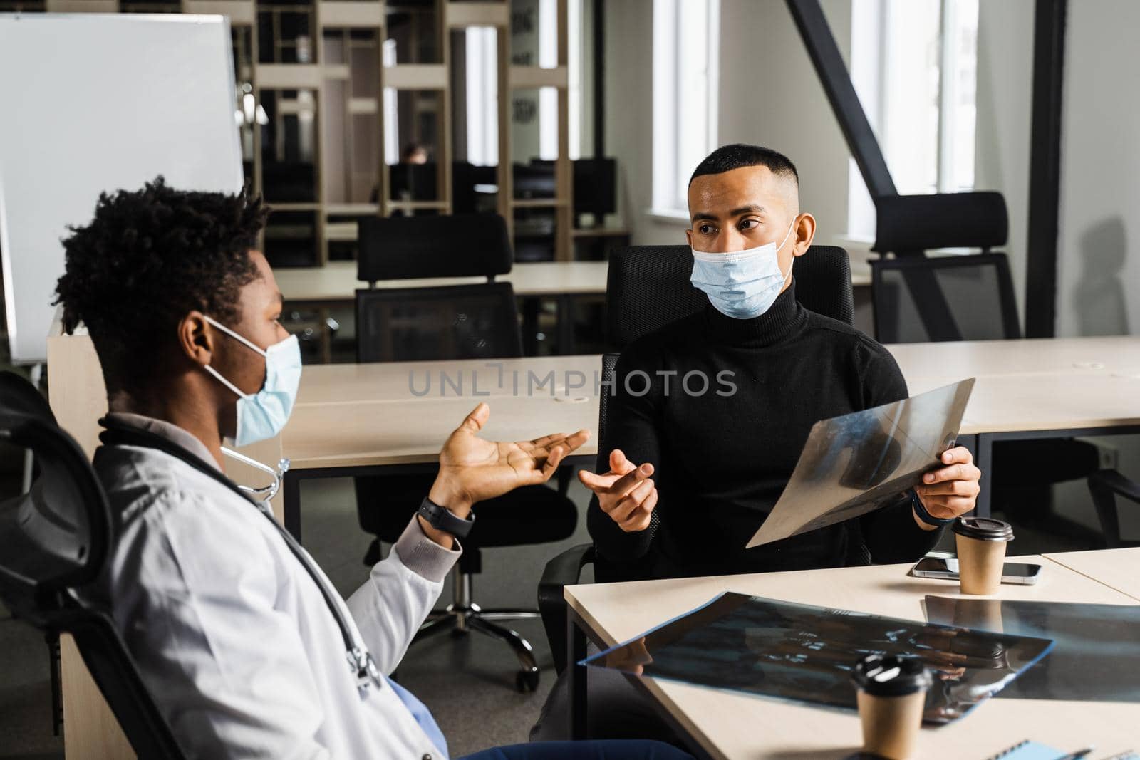 Handsome asian patient with x-ray image of fracture of foot bones at black doctor consultation. African surgeon discussing x-ray with patient