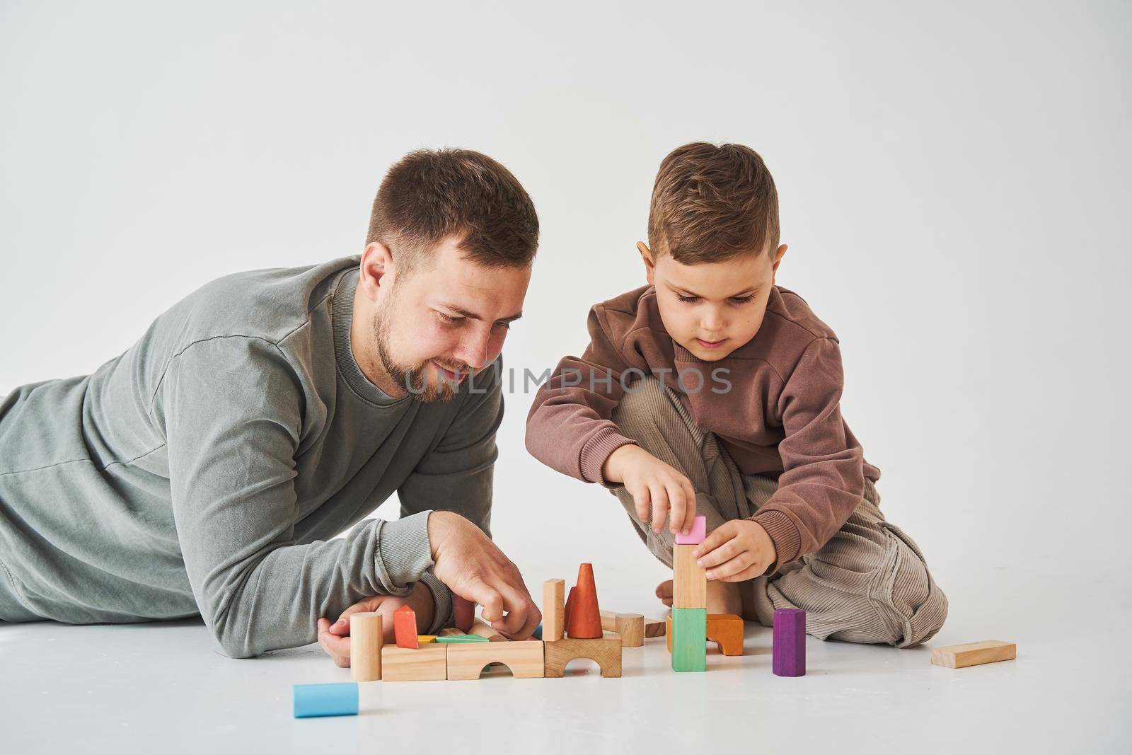 Caring dad plays with cheerful son with toy wooden cubes on white background. Fatherhood and child care