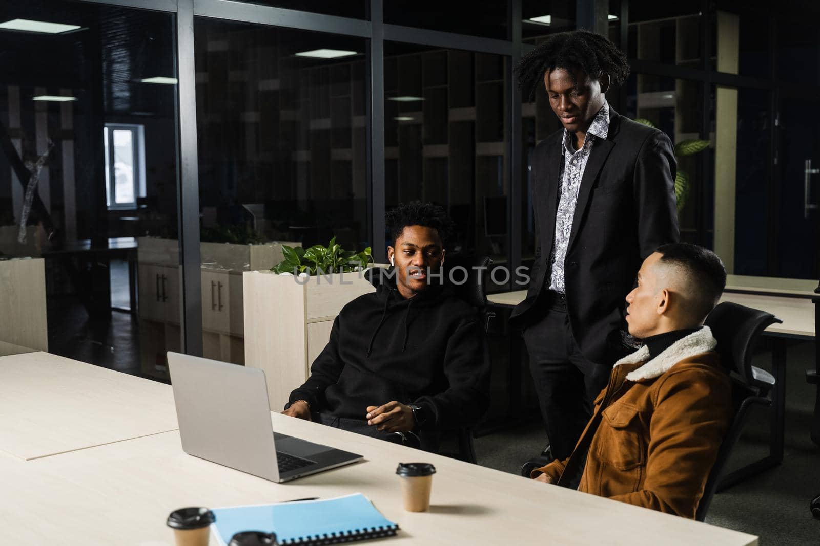 Multiethnic group of African and Asian colleagues are working on laptop on business project. Two black handsome managers teamwork with an Asian man and create creative ideas. by Rabizo