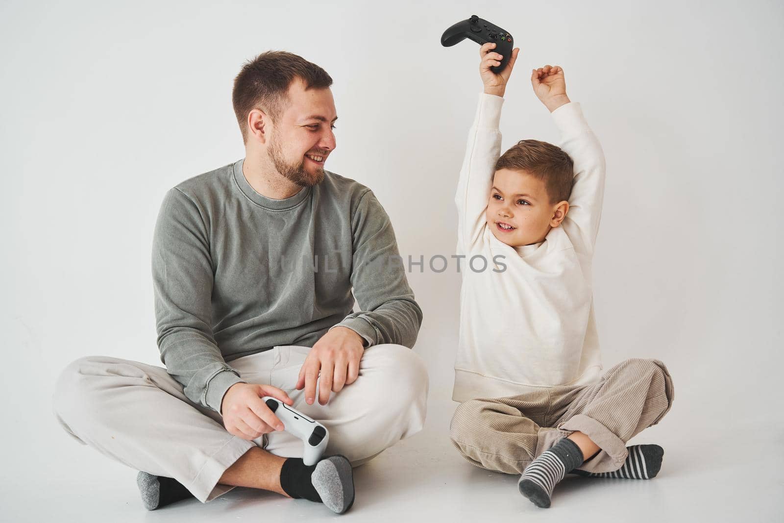 Son won father in game on console. Happy child with gamepad raises his hands up and rejoices in the victory in the game