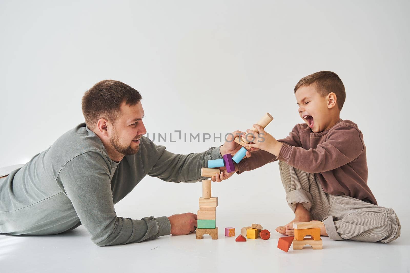 Dad and son smiling, having fun and playing colored bricks toy on white background. Paternity. Caring father with his child. by Rabizo