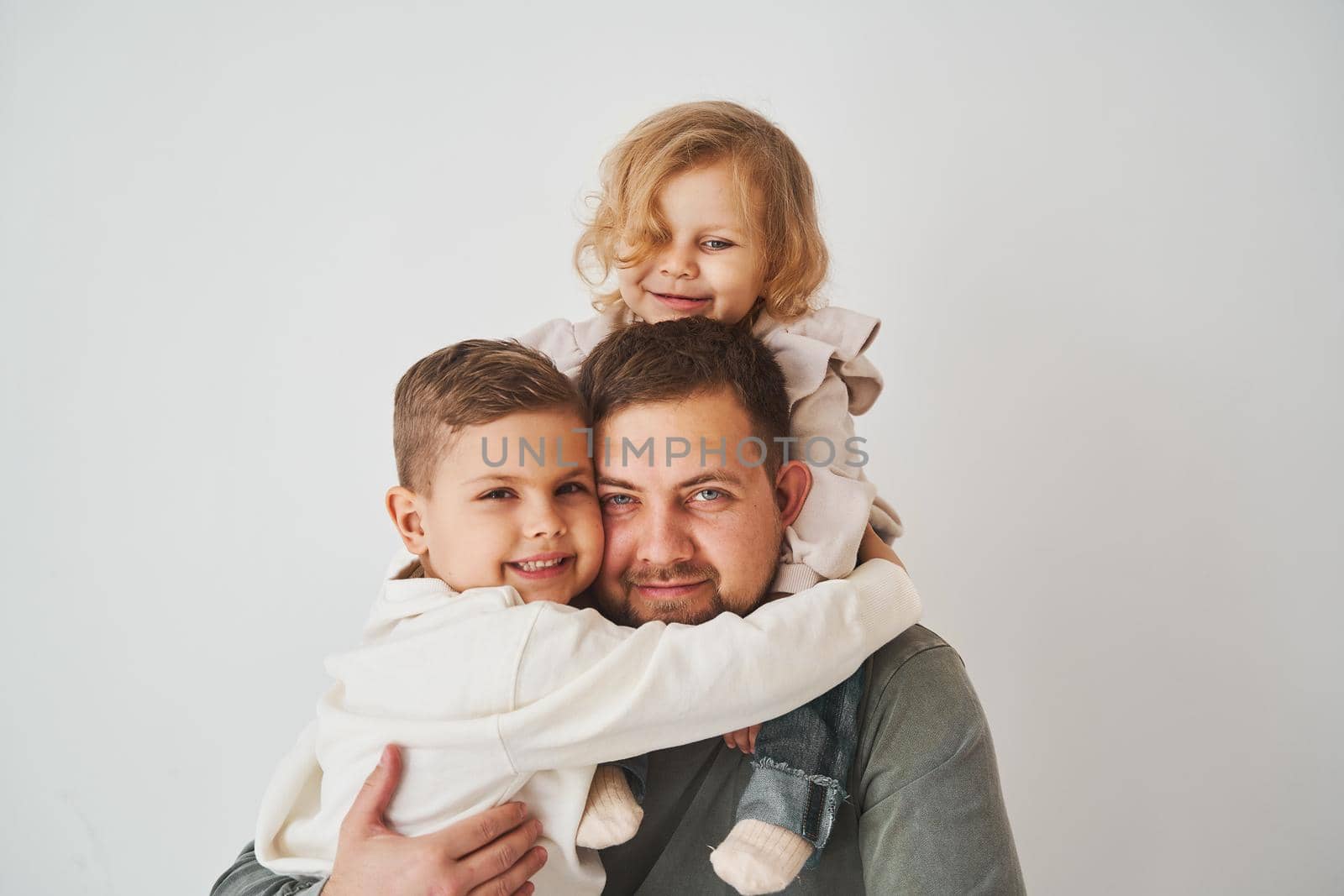 Close-up portrait of father, son and daughter. Happy family hugging and smiling on white background. Paternity. Single father bring up his children. by Rabizo