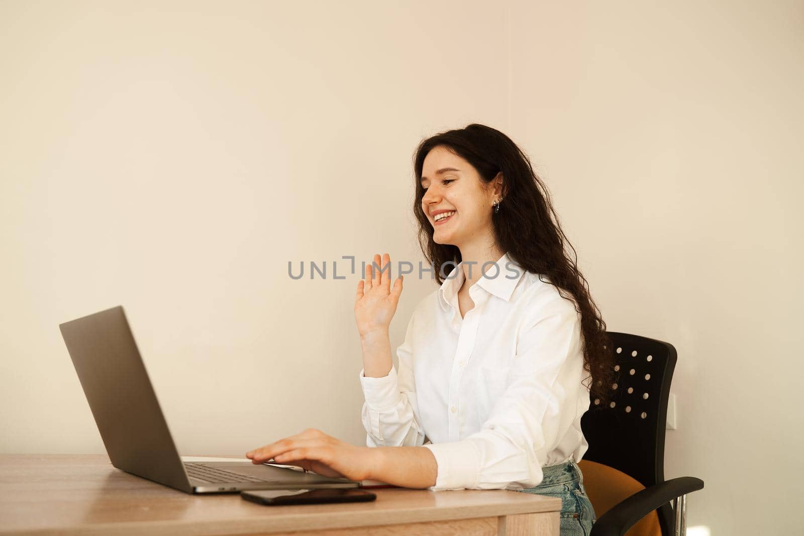 Positive caucasian girl enjoying friendly video call on laptop computer using web camera for communicating. Young woman waves her hand and greets her friends by video call. by Rabizo