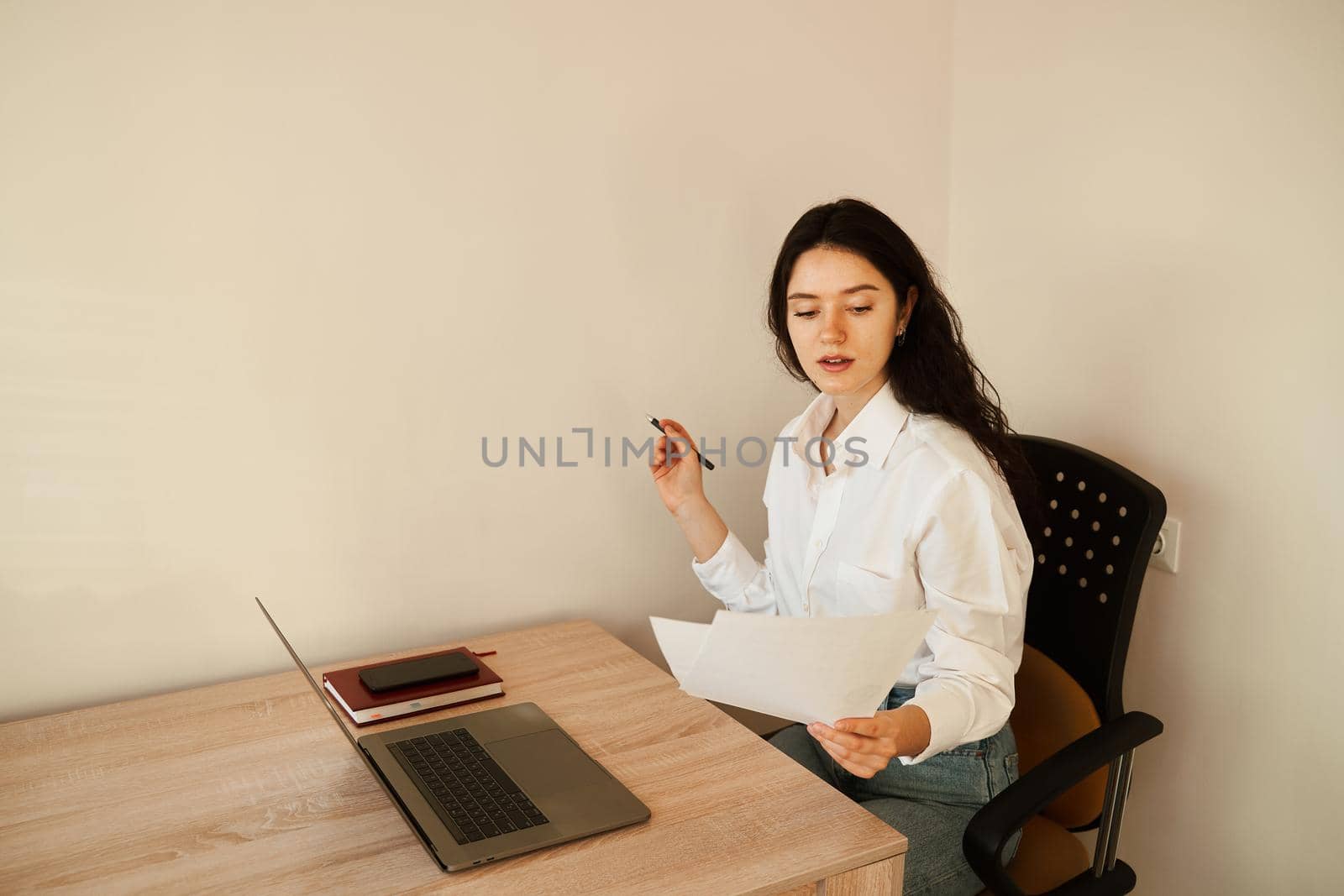 Attractive girl student studying online using laptop at home. Online education and distance learning. Girl holding papers in hands