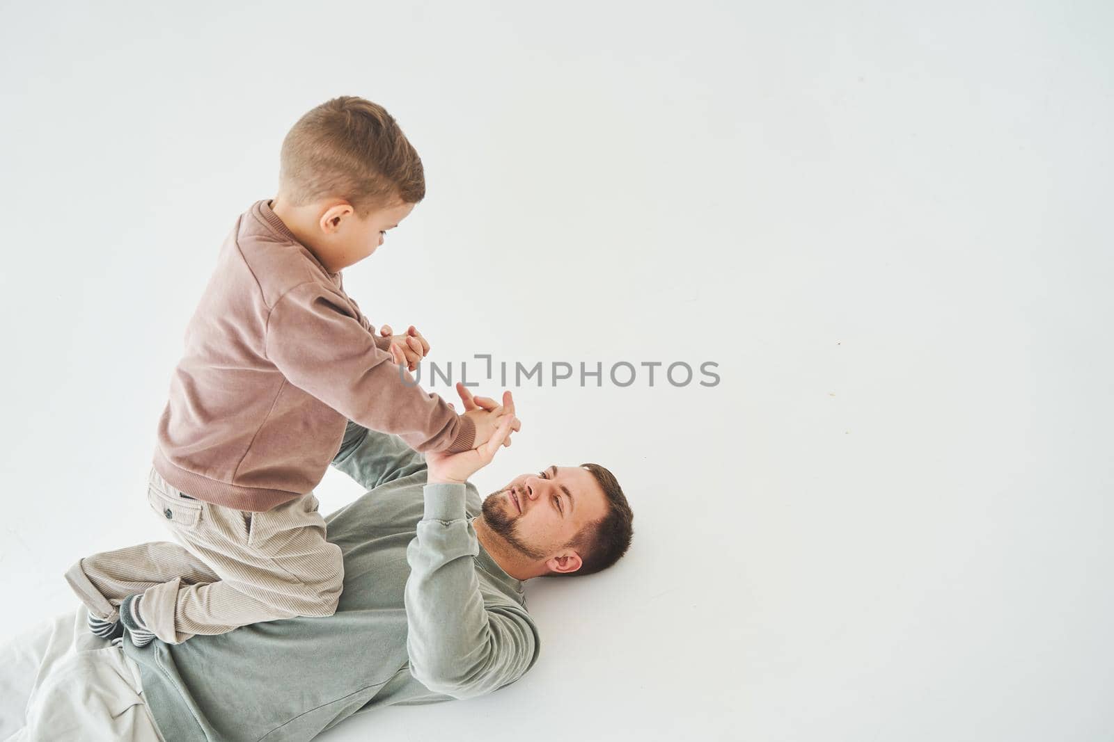 Father and son have fun and fool around together on white background. Child laughs with dad. Fatherhood. Child care. by Rabizo