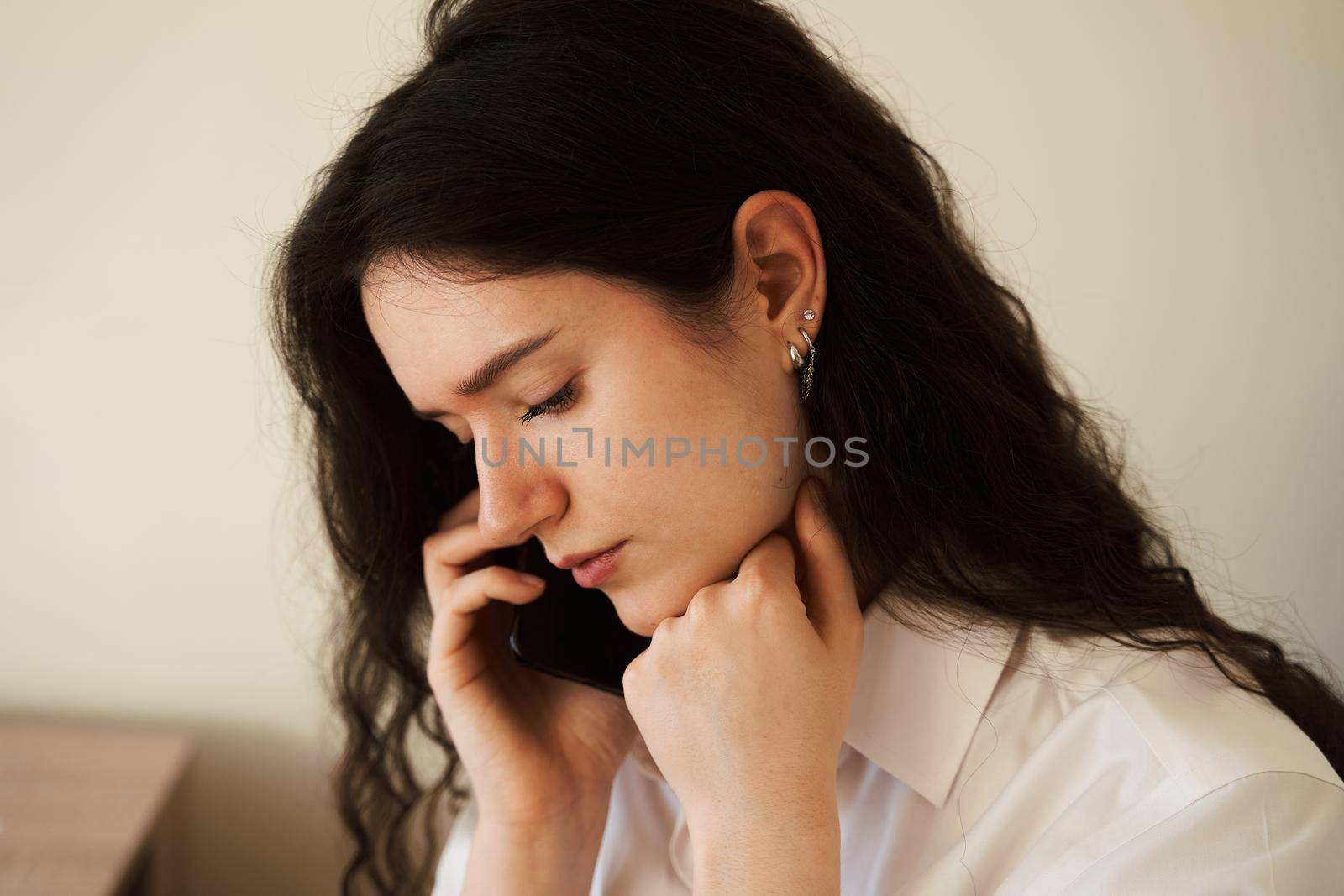 Sad and tired girl talking on the phone. Concept of chronic fatigue at remote online work. Stressful feelings due to overtime work. by Rabizo