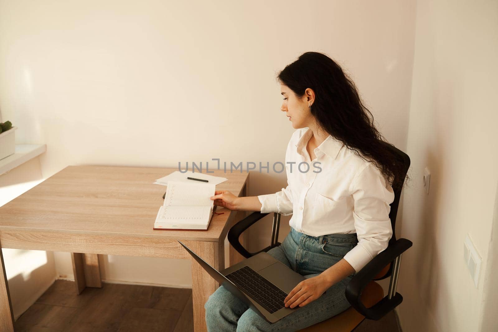 Attractive girl with laptop and papers working online and write notes on paper and talking by phone. Confident business woman work at home