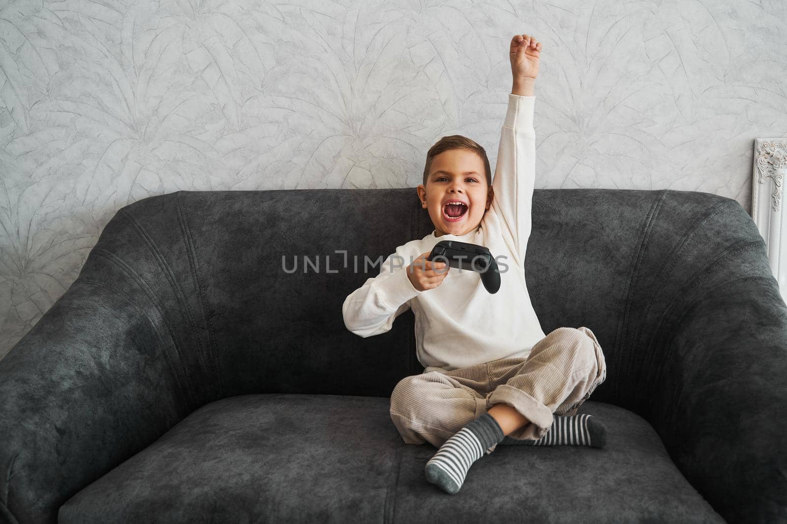 Emotional child with a gamepad rejoices, shouts and raises his hands up because he won the game. Happy boy play games at home