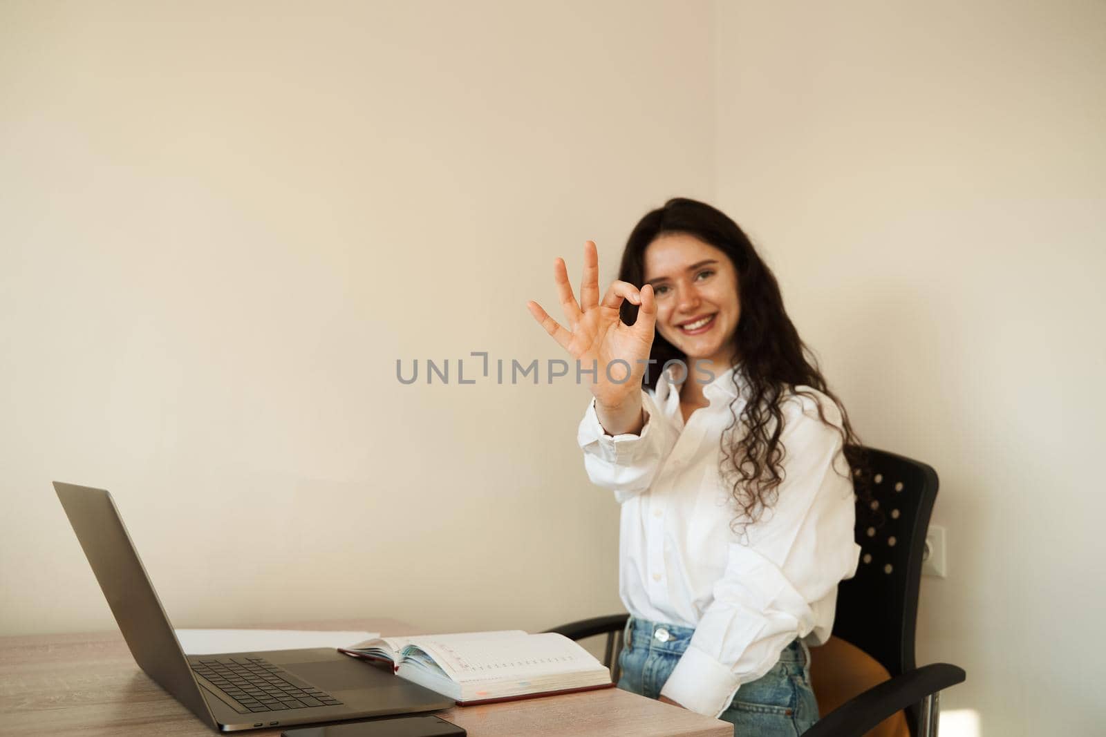Girl student showing ok sign. Schoolgirl with laptop done homework online and gesturing okay sign at table at home. by Rabizo