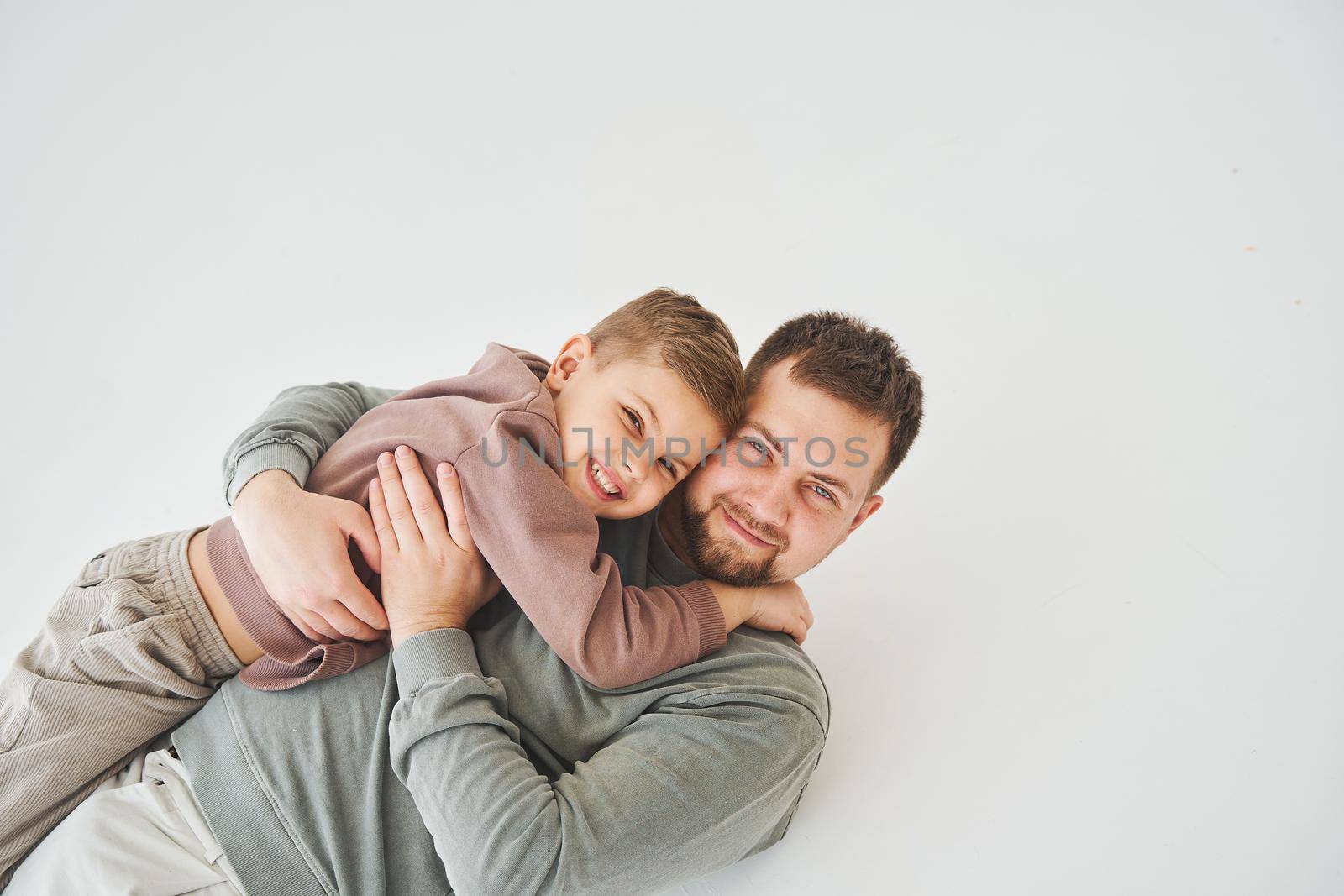 The son lies on the shoulder of his father. Dad hugs his child and smiles. Child care
