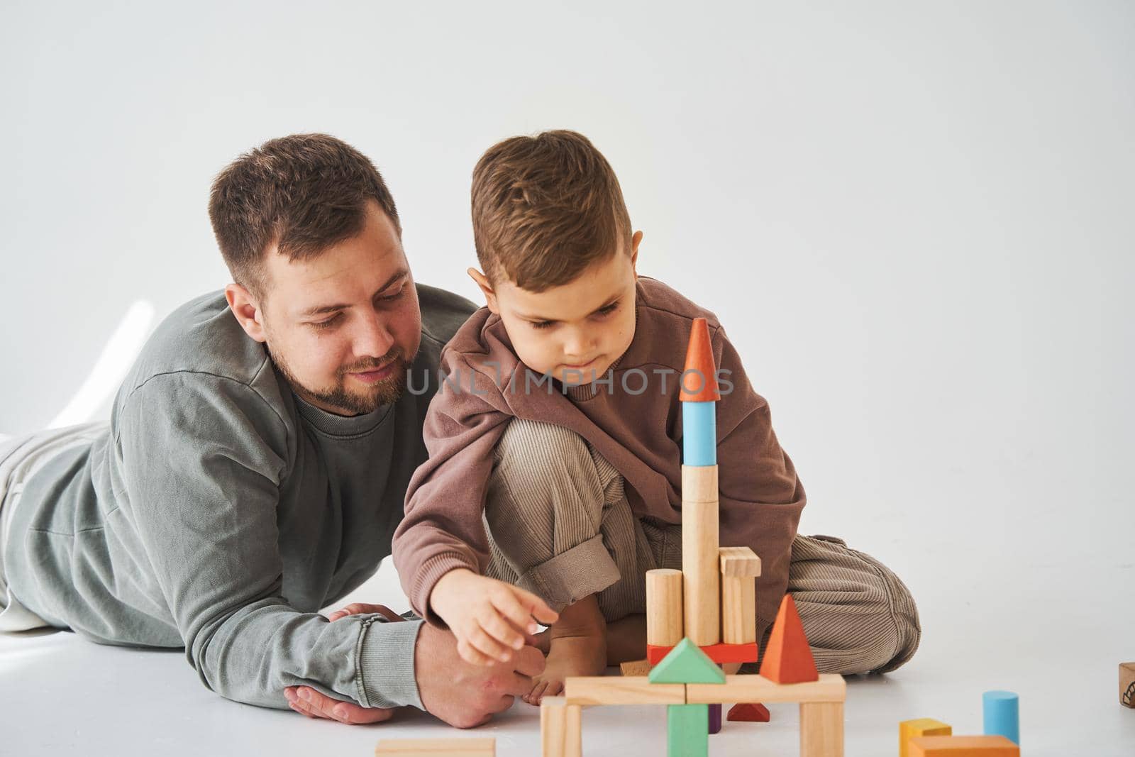 Paternity. Son and dad playing with colored bricks toy on white background. Father takes care of his kid