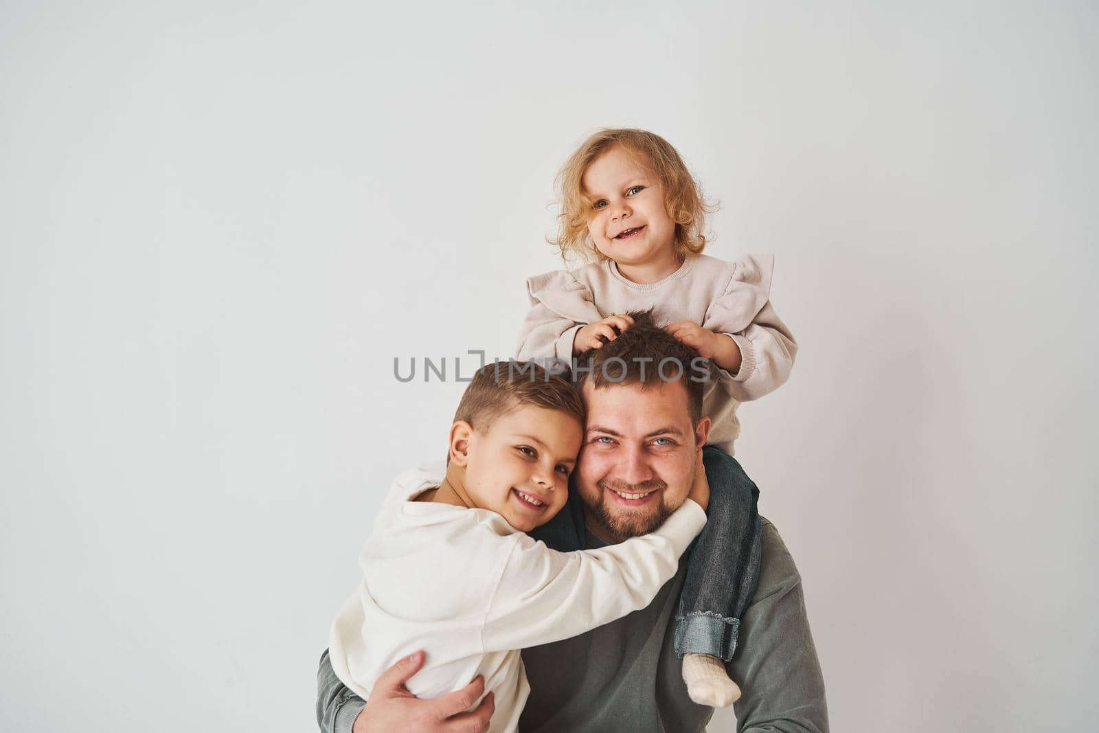 Close-up portrait of father, son and daughter. Happy family hugging and smiling on white background. Paternity. Single father bring up his children