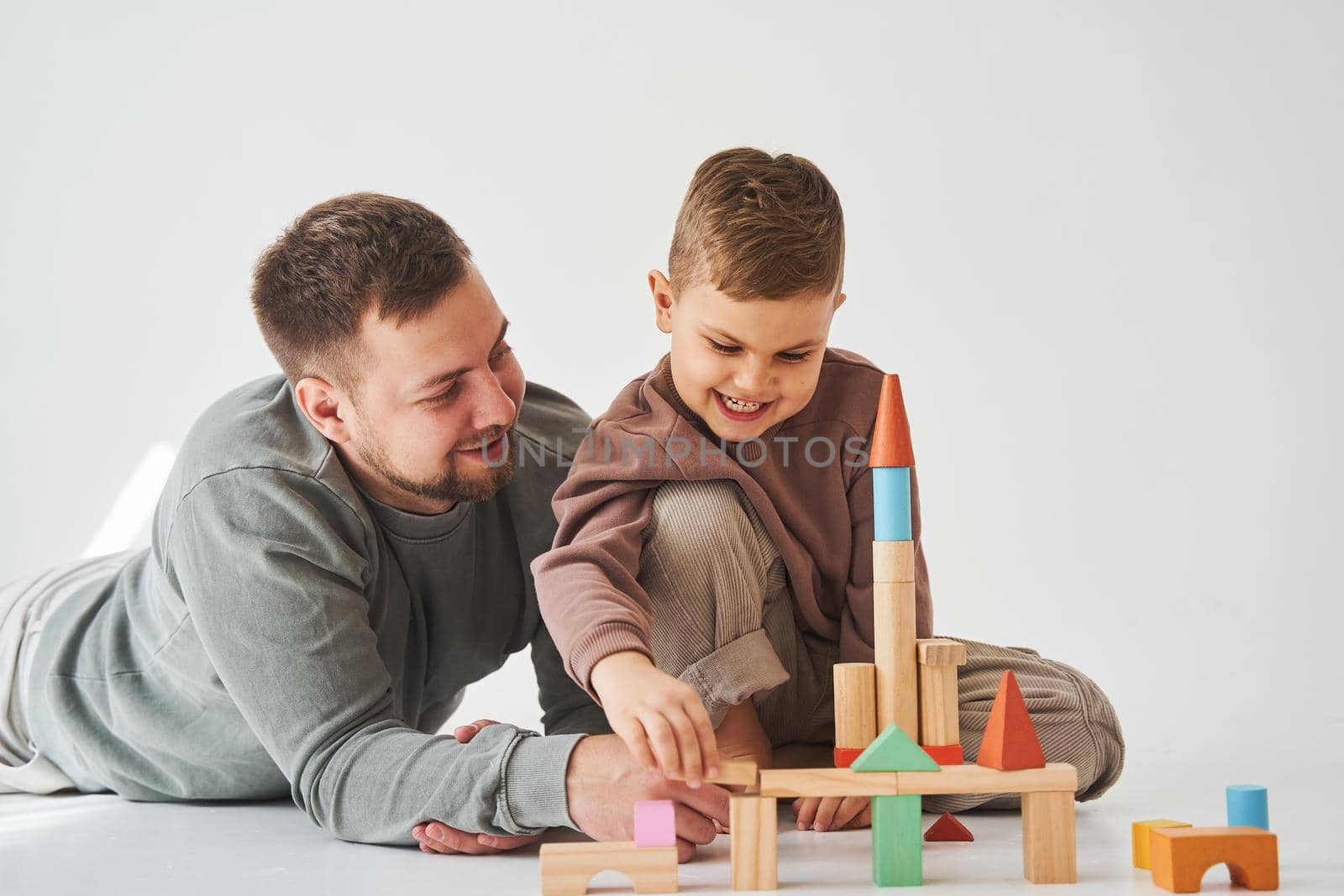 Paternity. Son and dad playing with colored bricks toy on white background. Father takes care of his kid. by Rabizo