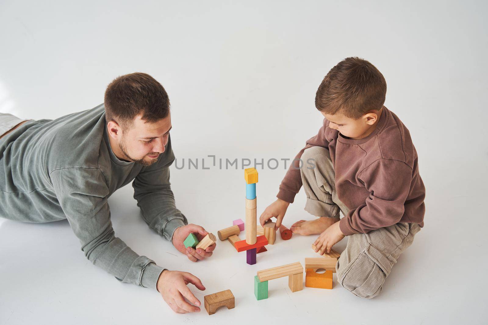 Caring dad plays with cheerful son with toy wooden cubes on white background. Fatherhood and child care