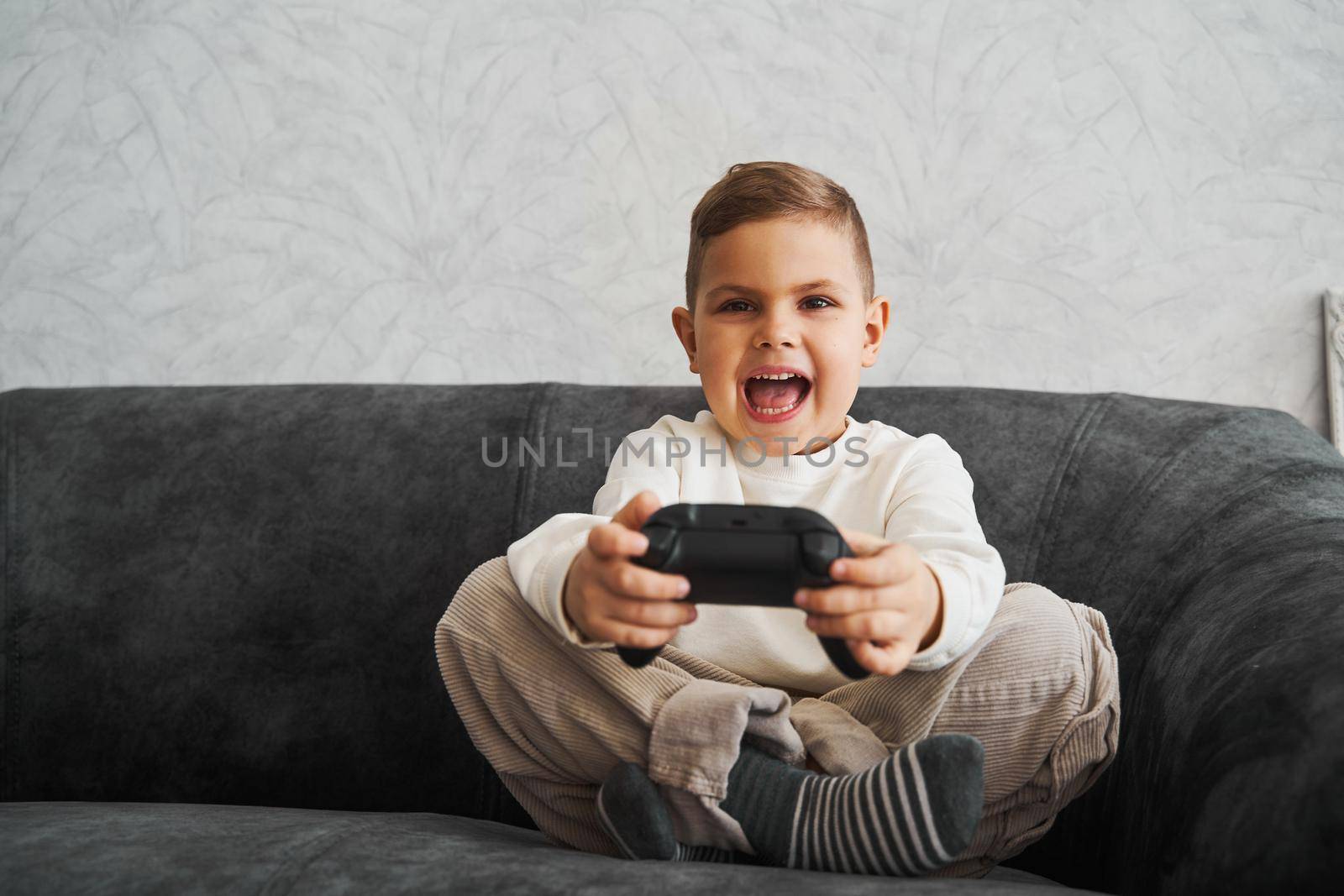 Surprised kid with gamepad playing console games at home. Gambling addiction of child. by Rabizo