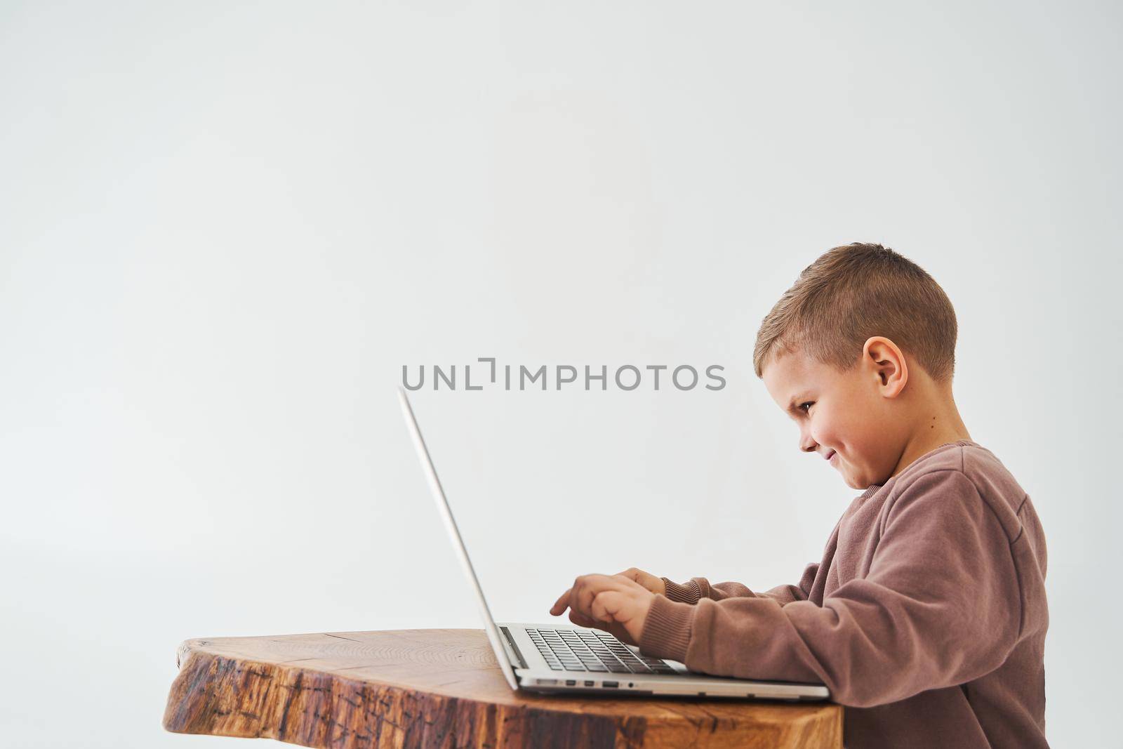 Handsome kid sitting at table, using laptop and looking at camera, watching virtual lecture and tutorial. E-learning and knowledge