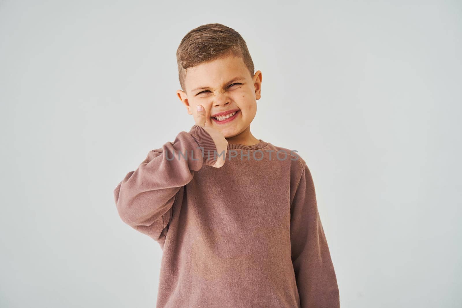 Happy child boy shows thumbs up and smiles on white background. Handsome kid posing and smiling