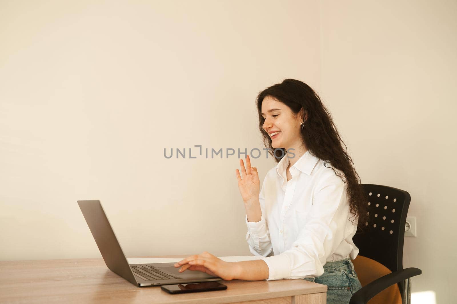 Positive caucasian girl enjoying friendly video call on laptop computer using web camera for communicating. Young woman waves her hand and greets her friends by video call. by Rabizo