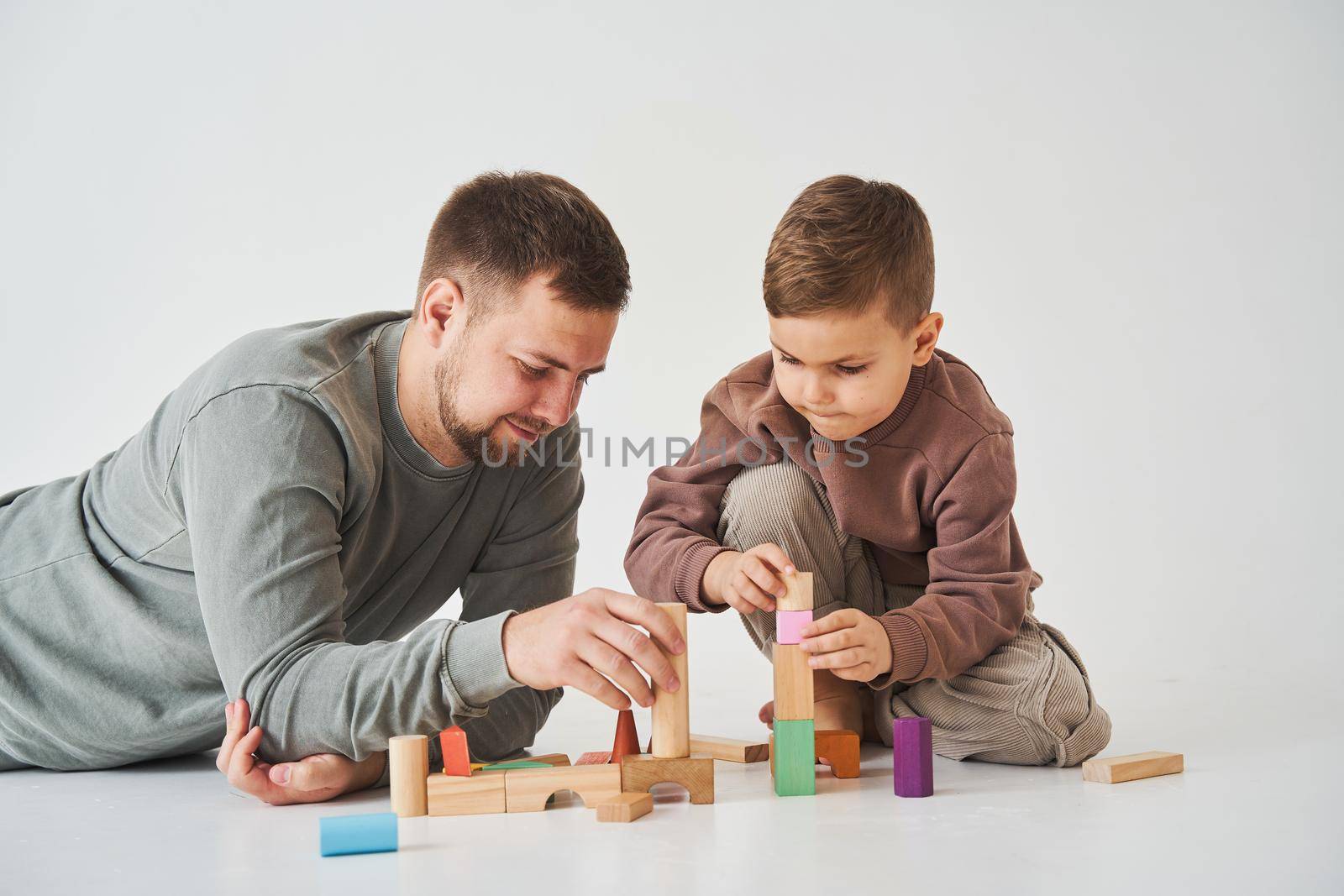 Caring dad plays with cheerful son with toy wooden cubes on white background. Fatherhood and child care