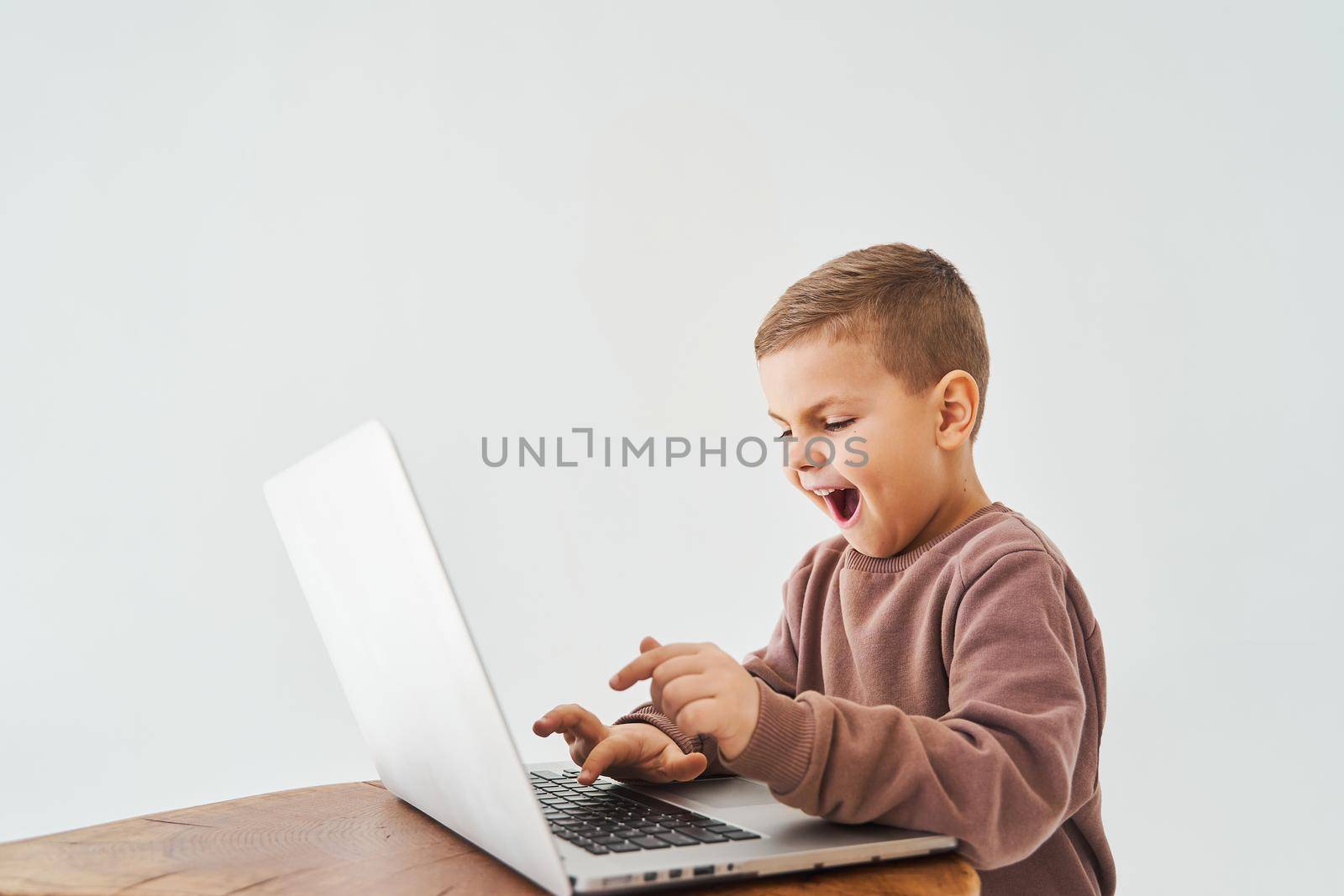 Emotional child play online games on laptop. Gambling addiction. Handsome kid gamer is gaming on laptop on white background