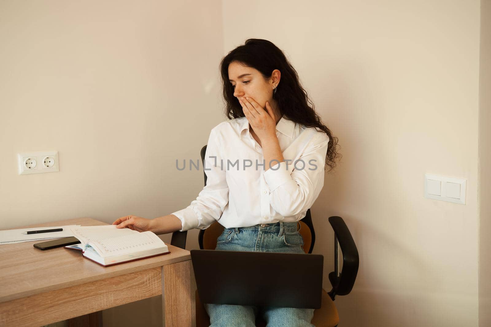 Attractive girl with laptop and papers working online and write notes on paper and talking by phone. Confident business woman work at home. by Rabizo