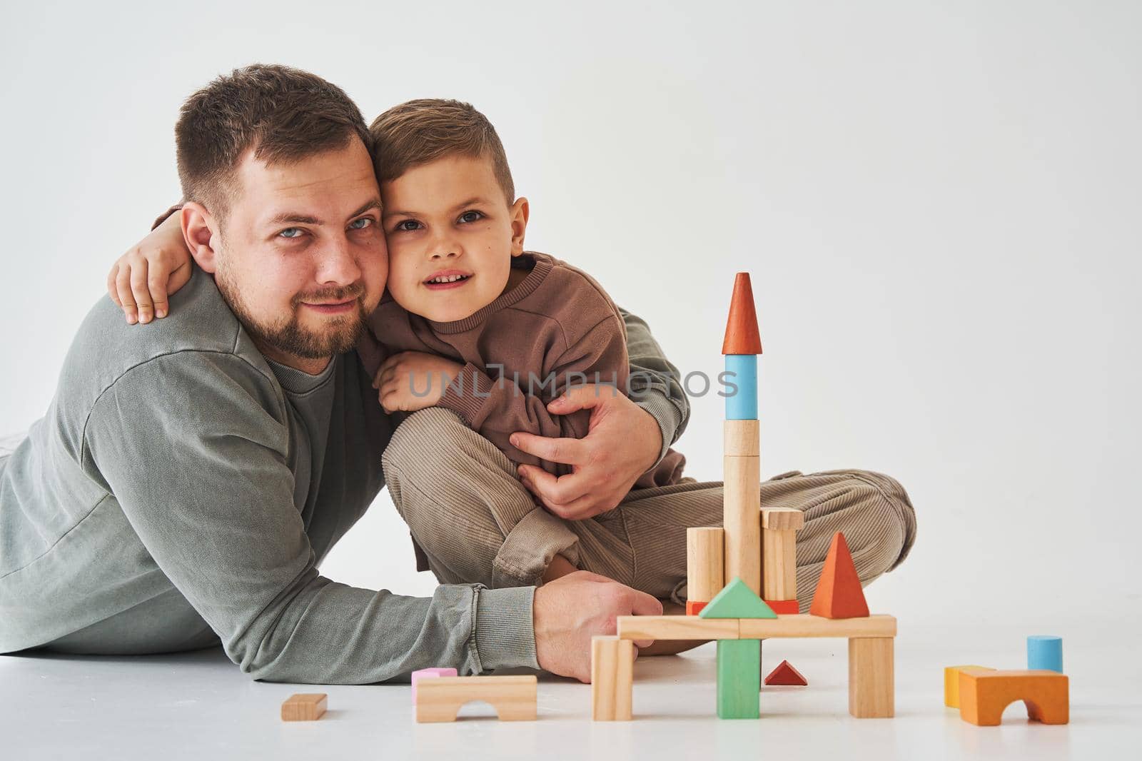 Paternity. Son and dad playing with colored bricks toy on white background. Father takes care of his kid. by Rabizo