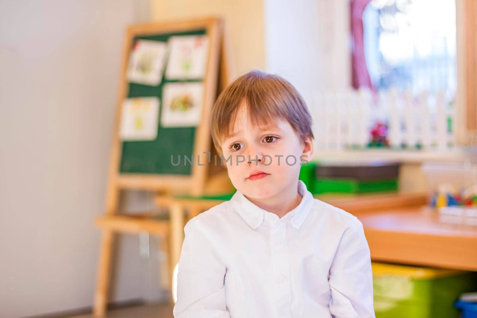 Elegantly dressed in a white shirt, a little boy is sitting in the classroom for lessons. portrait of a boy, blonde hair