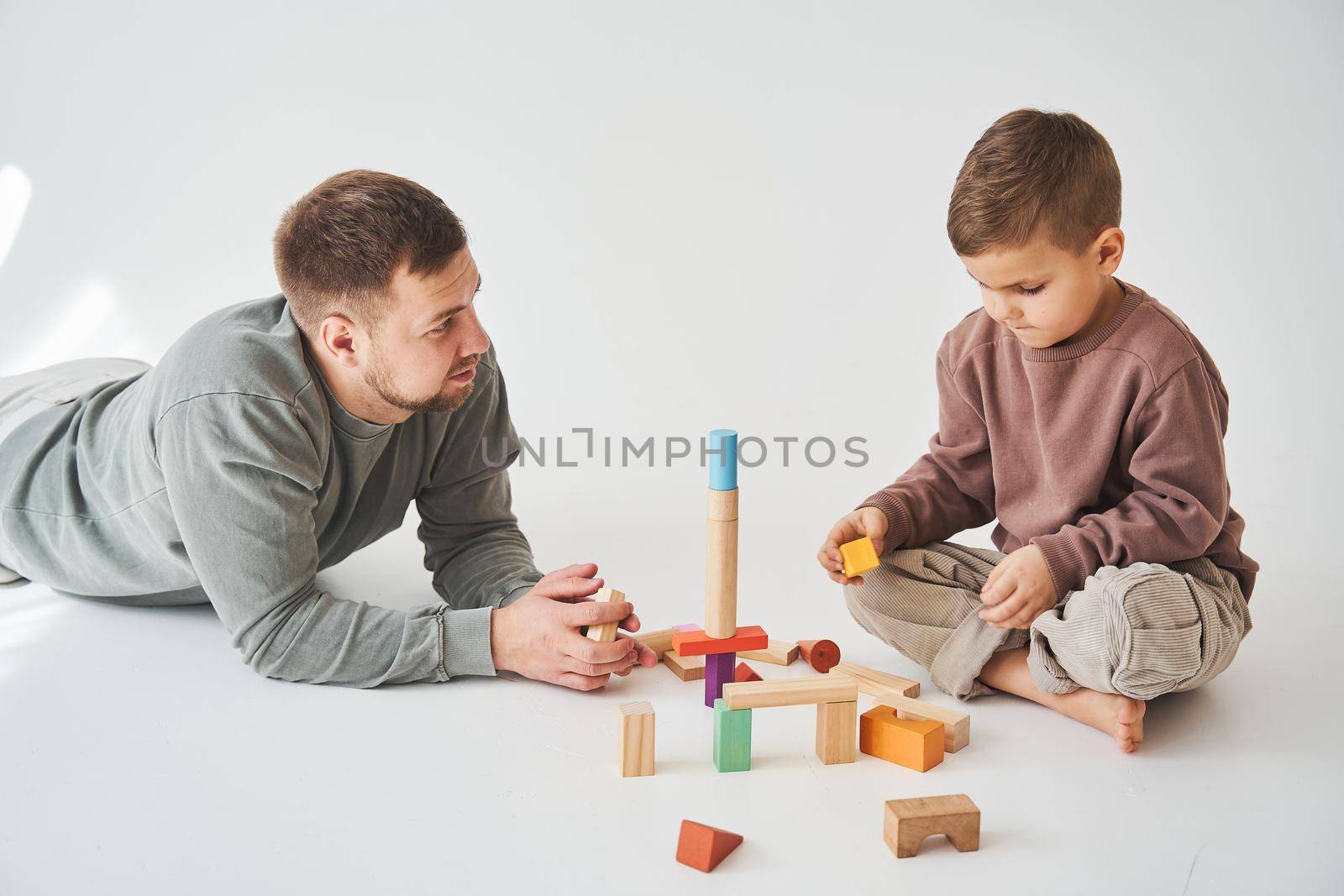 Caring dad plays with cheerful son with toy wooden cubes on white background. Fatherhood and child care
