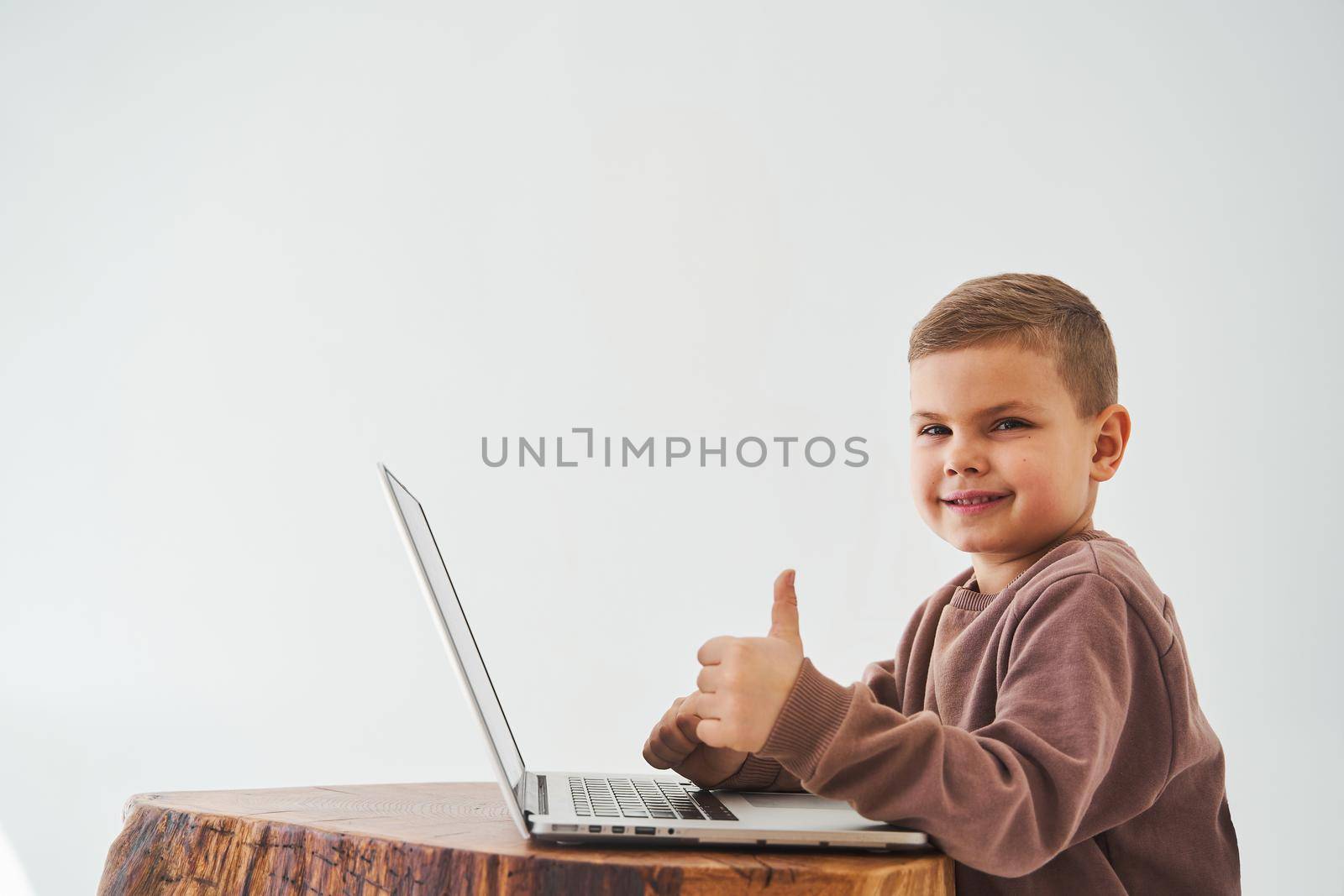 Child boy study online with laptop and shows thumbs up and smiles. Online education and e-learning. Child taking online courses on laptop. by Rabizo