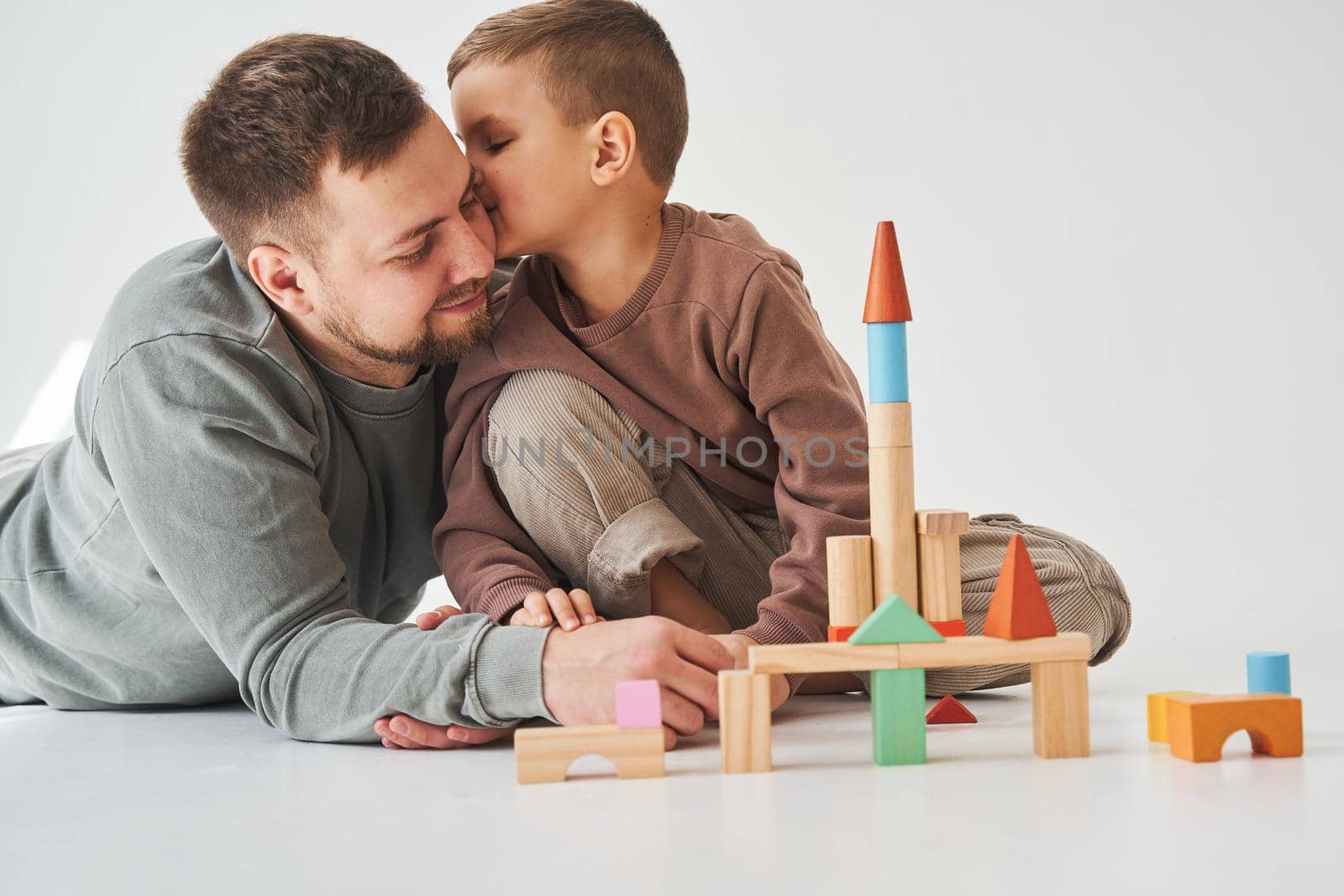 Handsome son kissing his father. Paternity. Dad and his son playing with colored wooden blocks on white background. by Rabizo