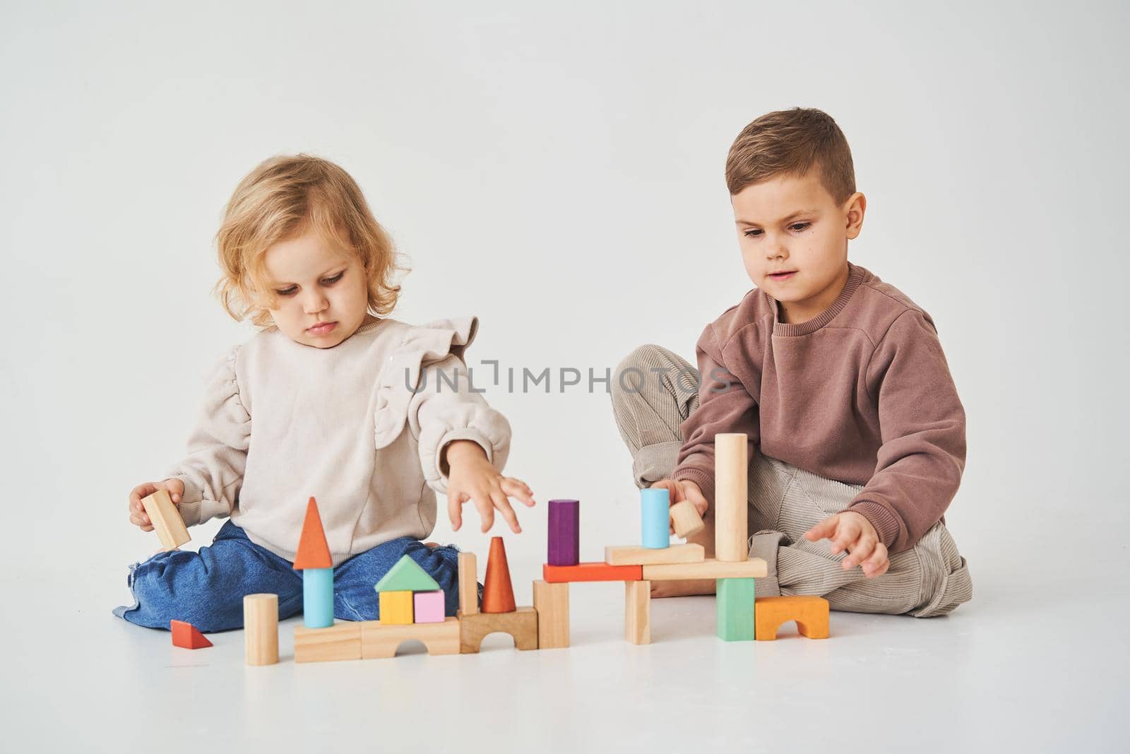 Child girl plays with cheerful kid with toy wooden cubes on white background. Children have smiling and have fun together