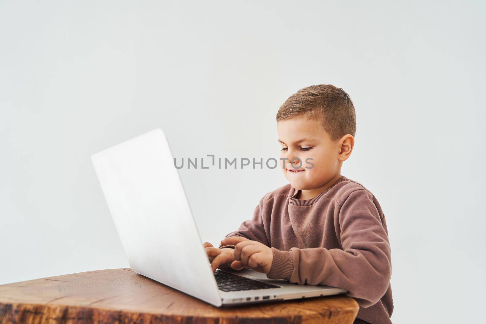 Handsome kid use laptop and look at camera, watch virtual lecture and tutorial. E-learning and knowledge. Preparation for lesson and studying online on white background