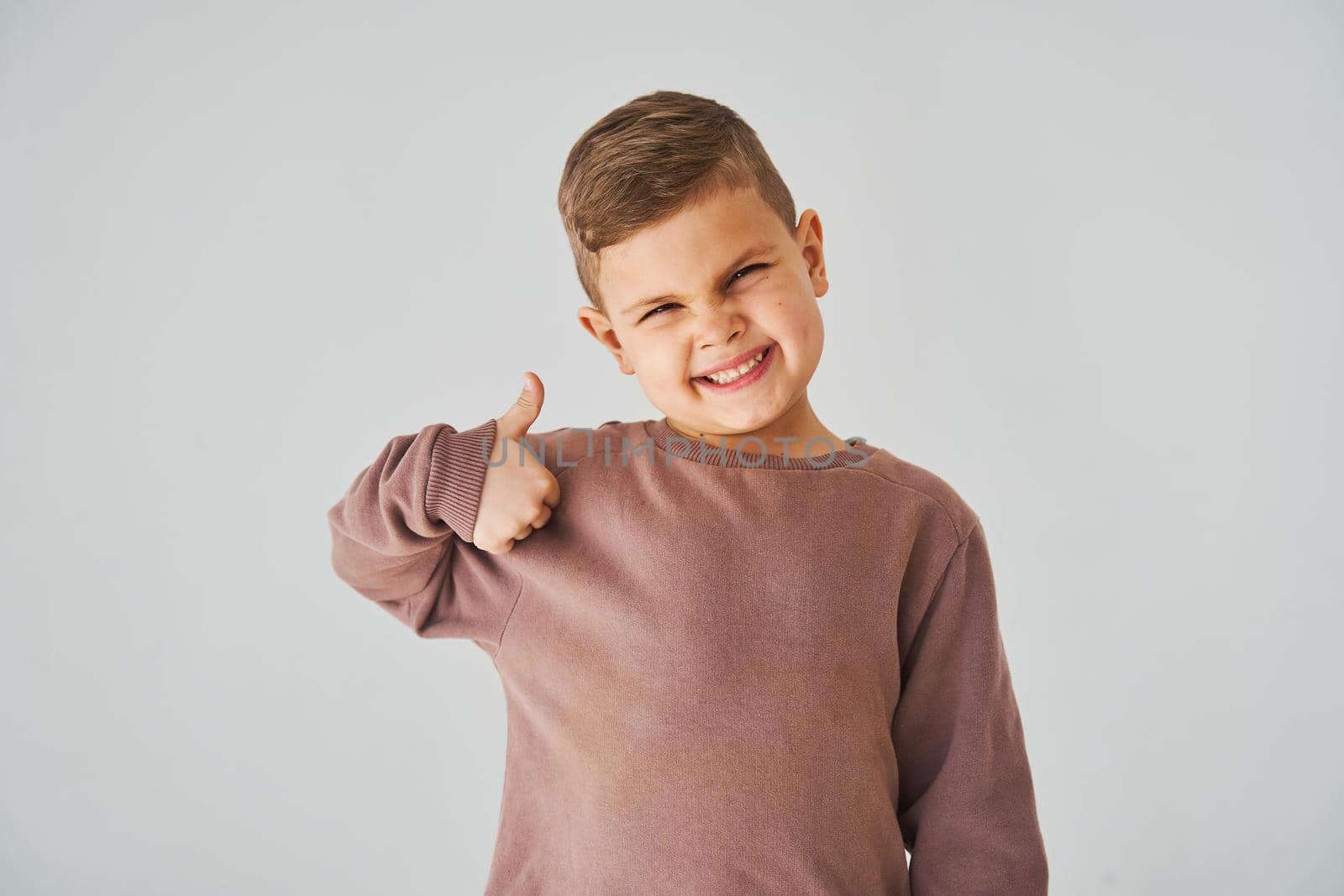 Happy child boy shows thumbs up and smiles on white background. Handsome kid posing and smiling. by Rabizo