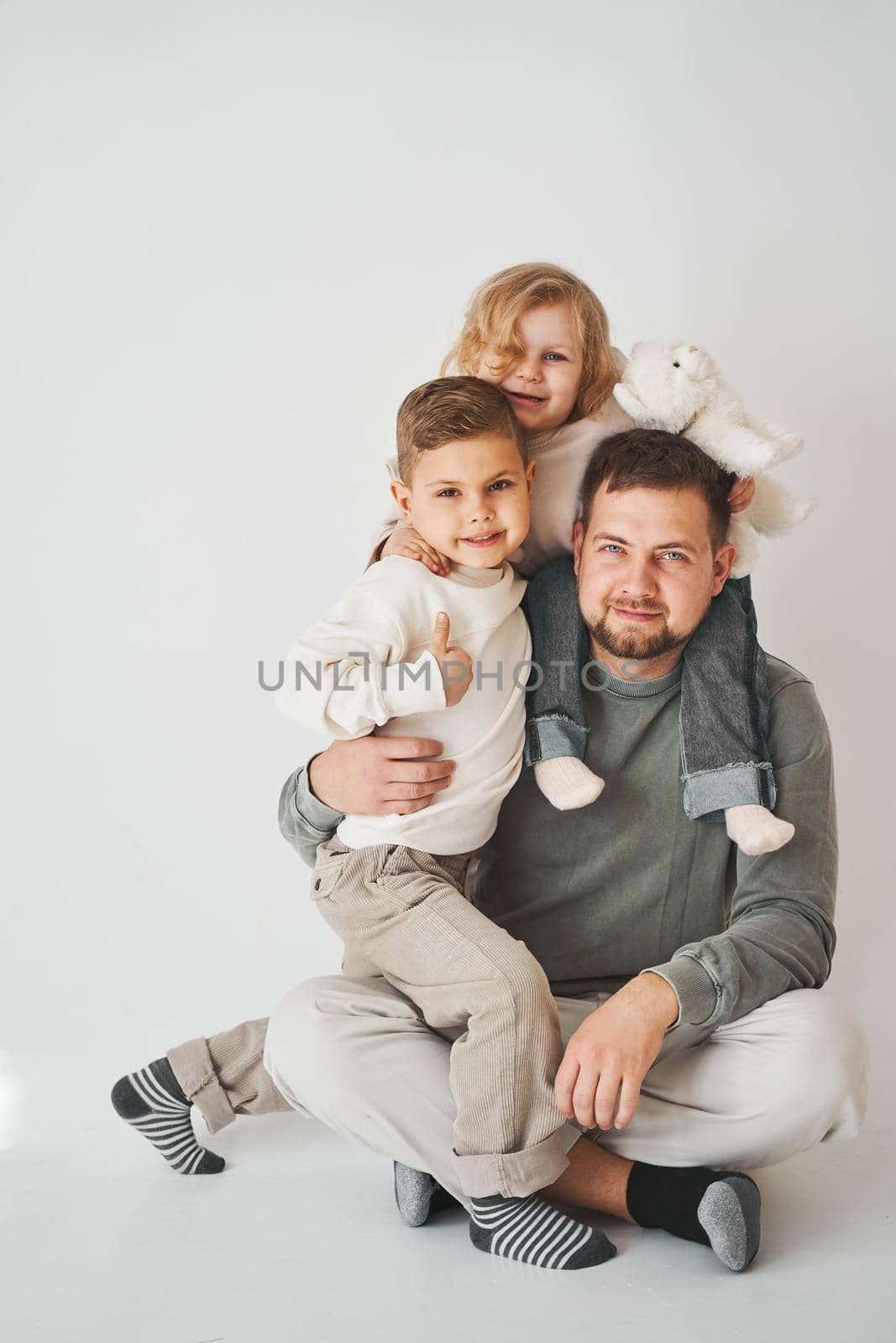 Happy family. Father, daughter and son hugging and smiling on white background. Paternity. Single father bring up his children. by Rabizo