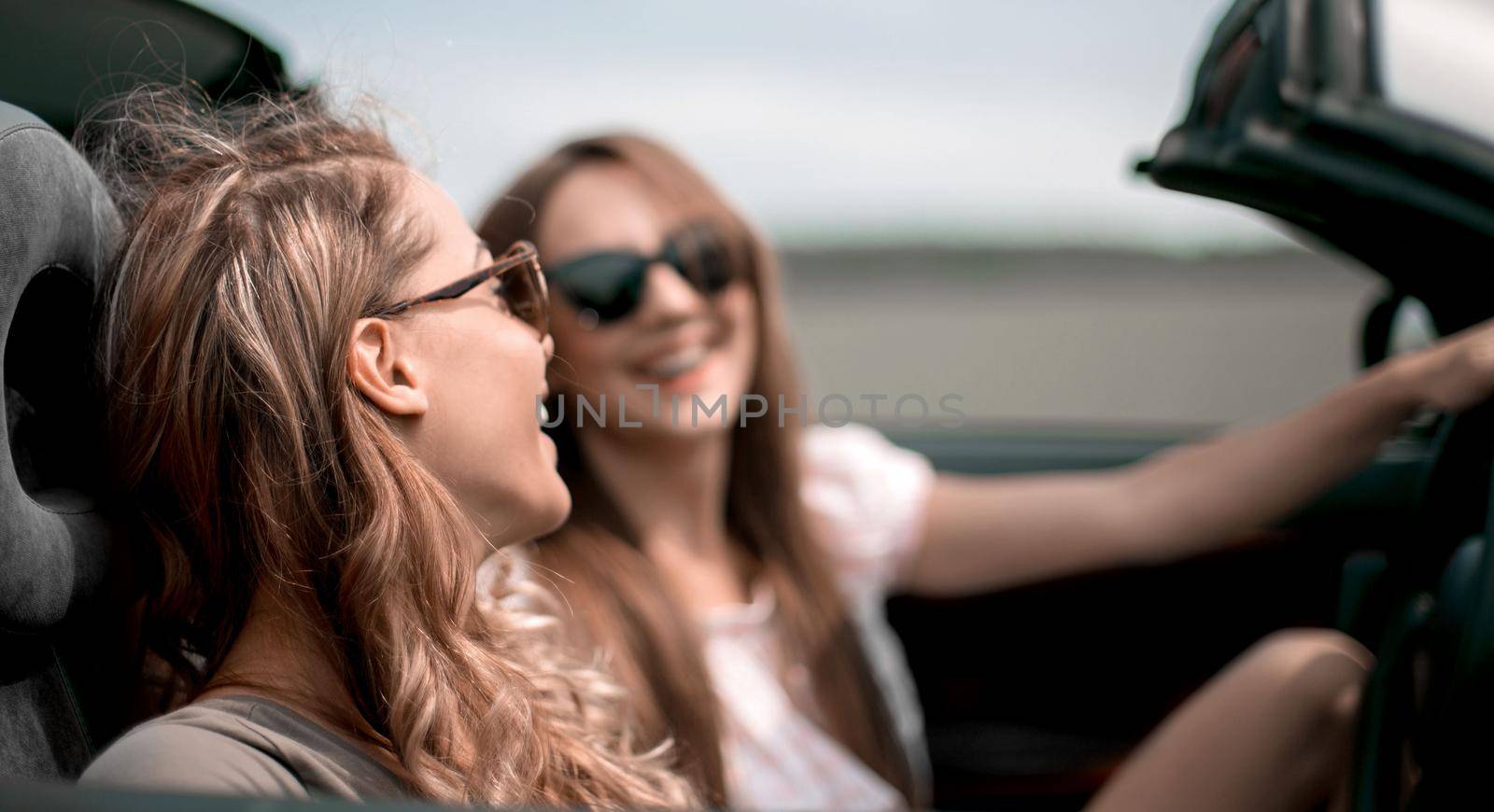 two fashionable girls travel in a convertible car. by asdf