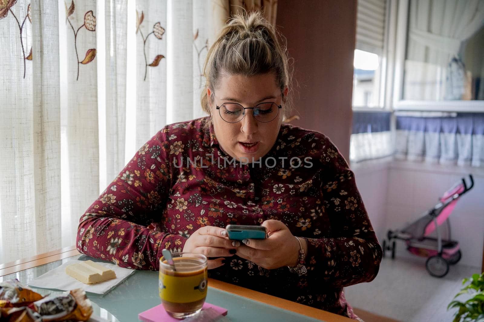 blonde woman, young with glasses, drinking coffee looking at smartphone