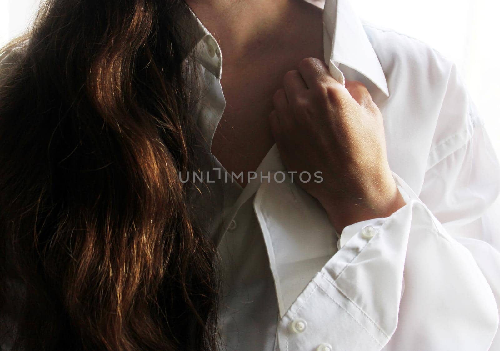 A beautiful brunette in a white shirt holds her hand to the collar of her shirt..