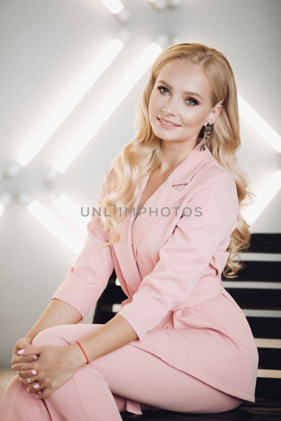 Blonde in pink smart suit sitting on stairs and posing by StudioLucky