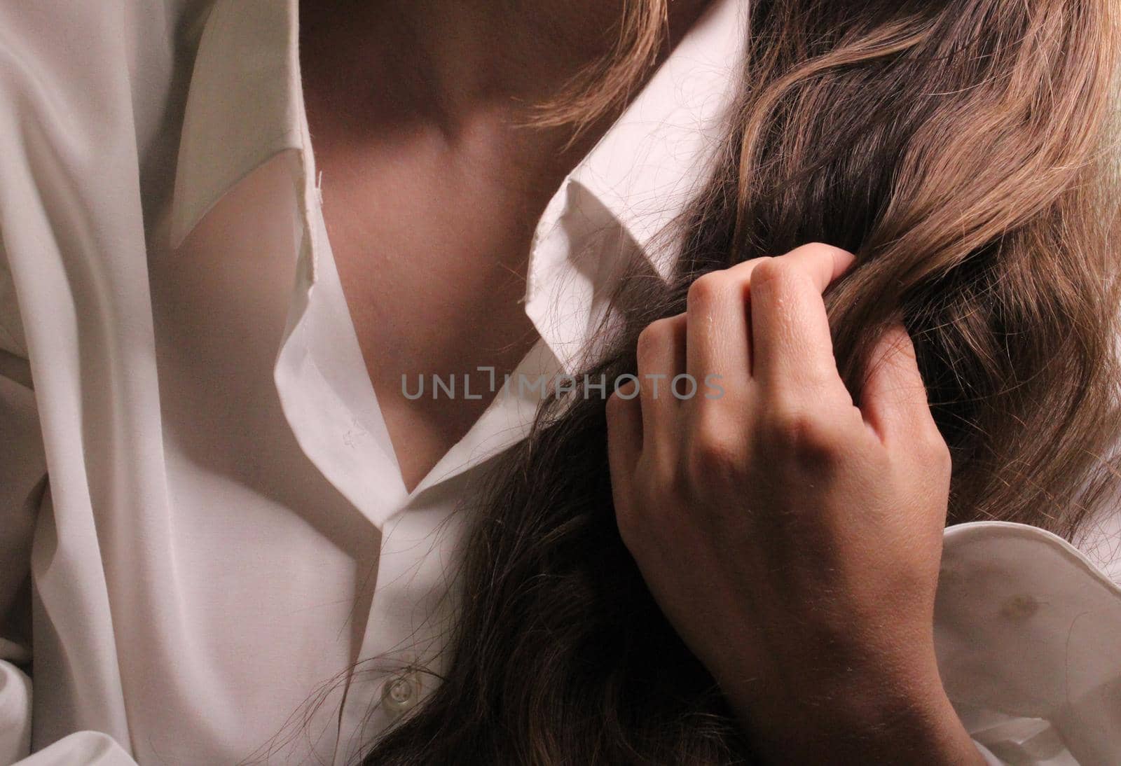 A beautiful girl in a white shirt holds long dark hair with her hand..