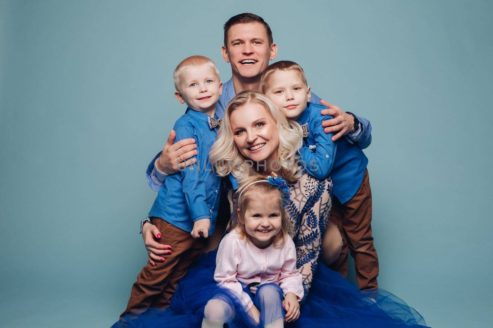 Studio portrait of happy smiling family of five posing and looking at camera together. Cheerful father embracing his children. Isolate on blue.