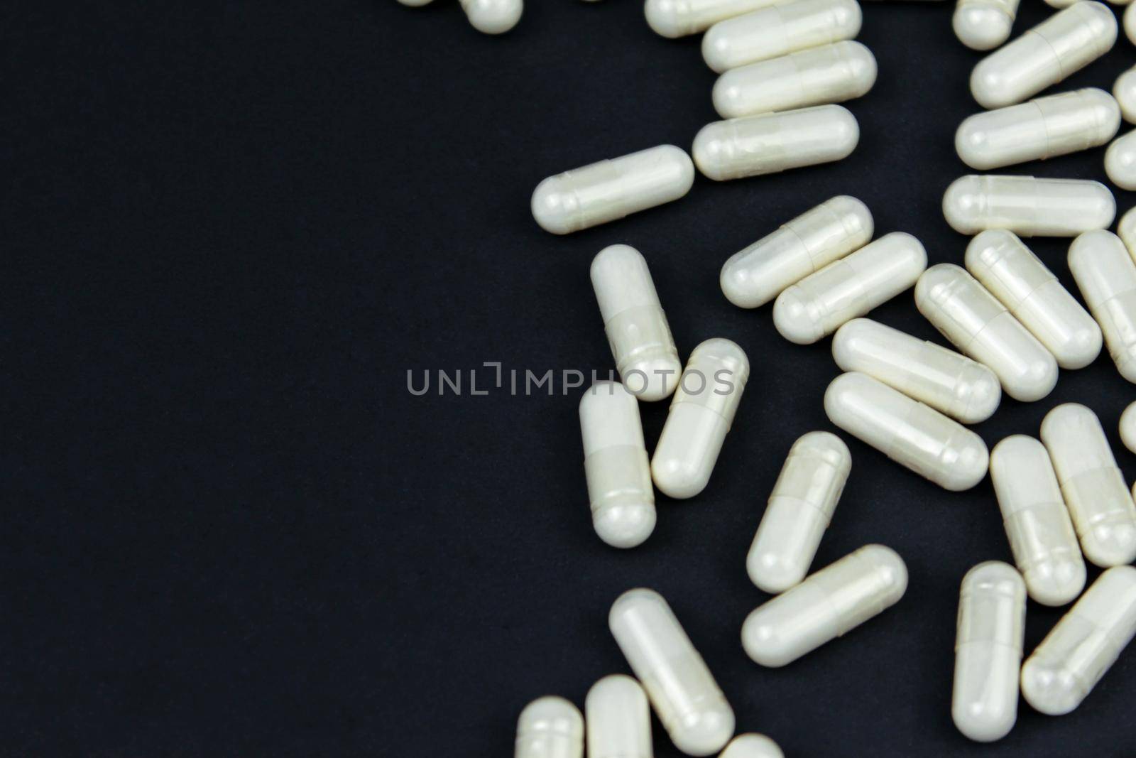 Heap of white medication and pills, capsules on black background. Top view, flat lay. Close-up.