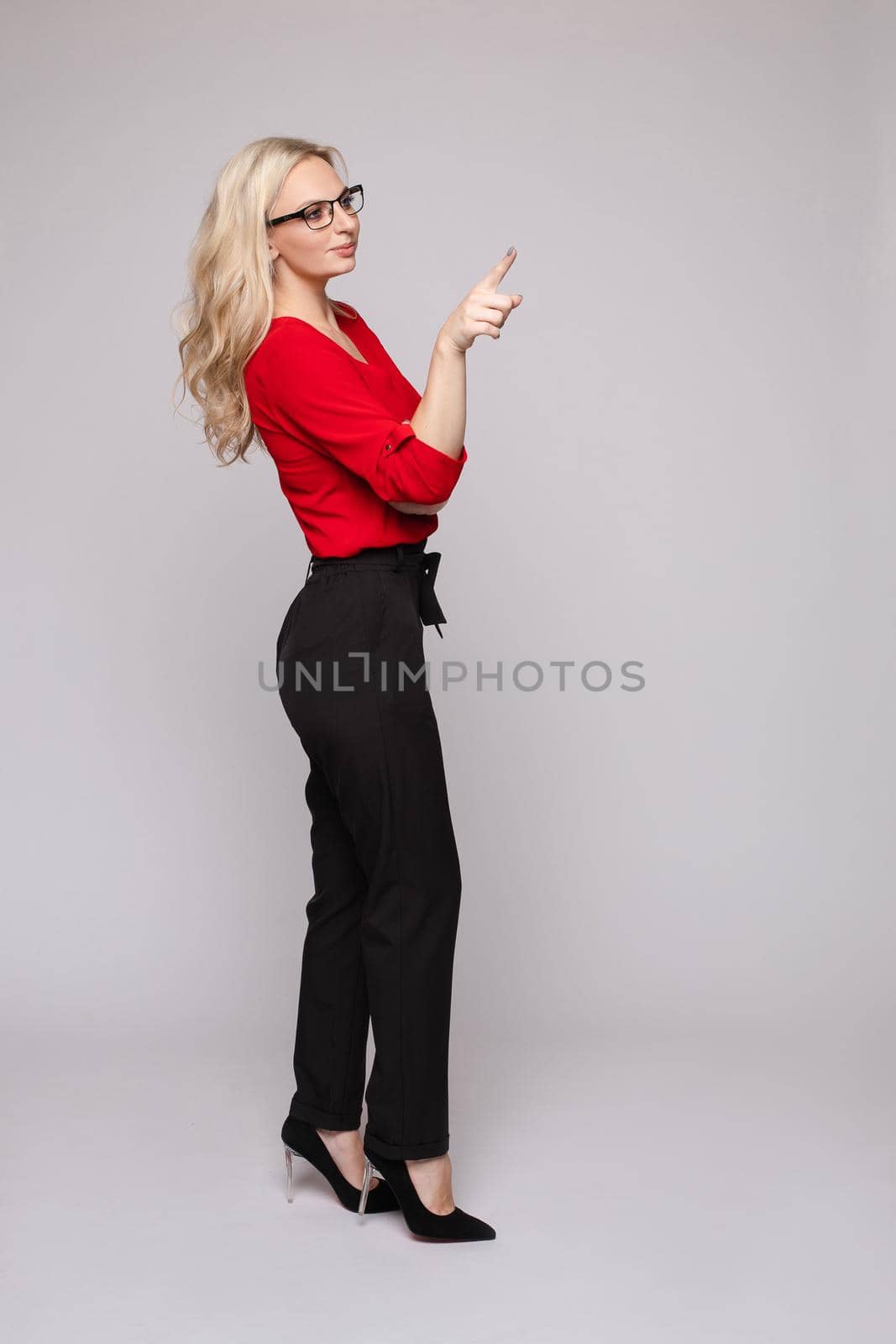 Front view of elegant successful female wearing smart outfit and glasses and posing on isolated background. Intelligent woman with folded arms looking at camera in studio. Concept of job and business.